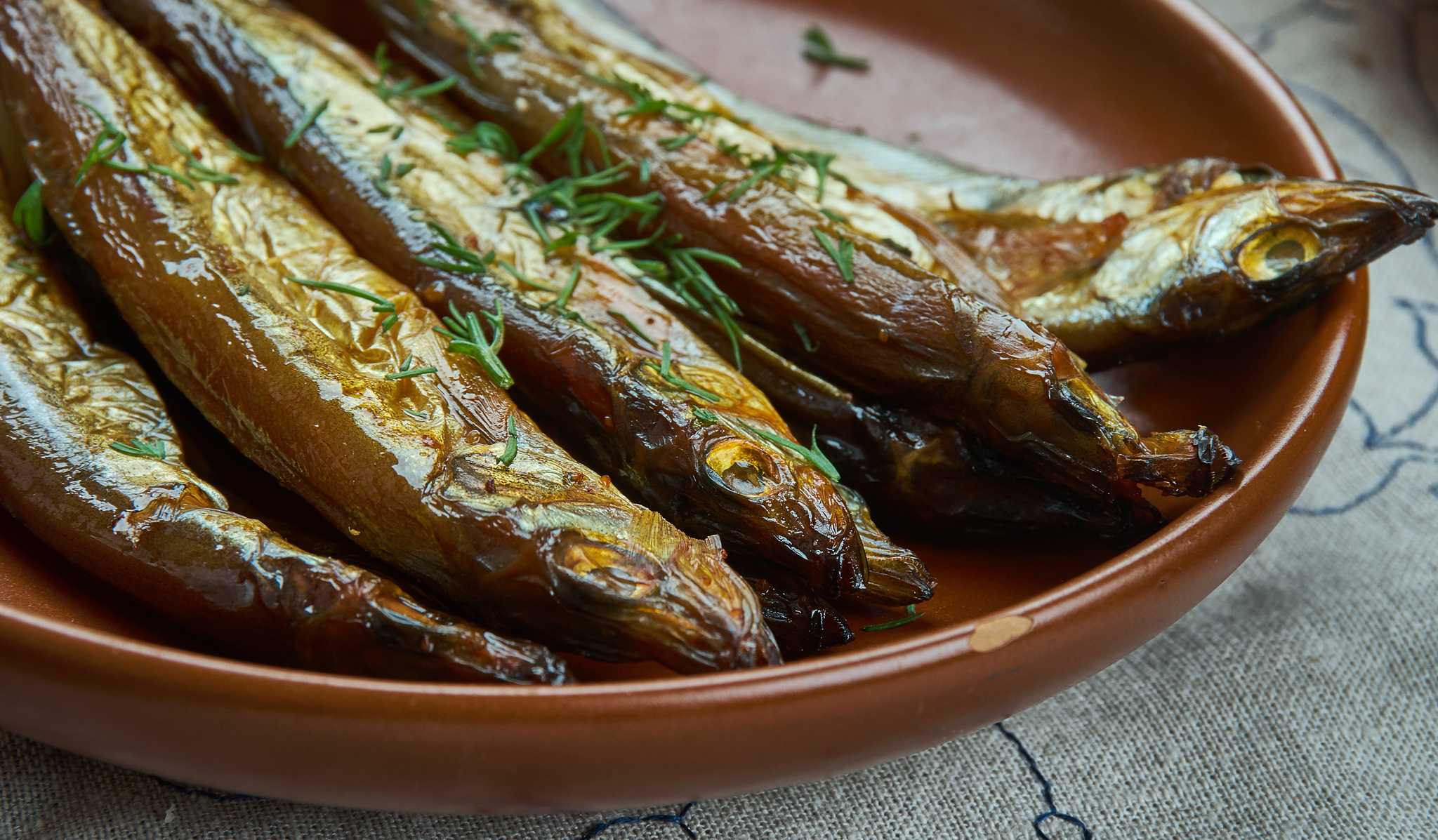 Small dried lake fish sprinkled with herbs on a terracotta plate.