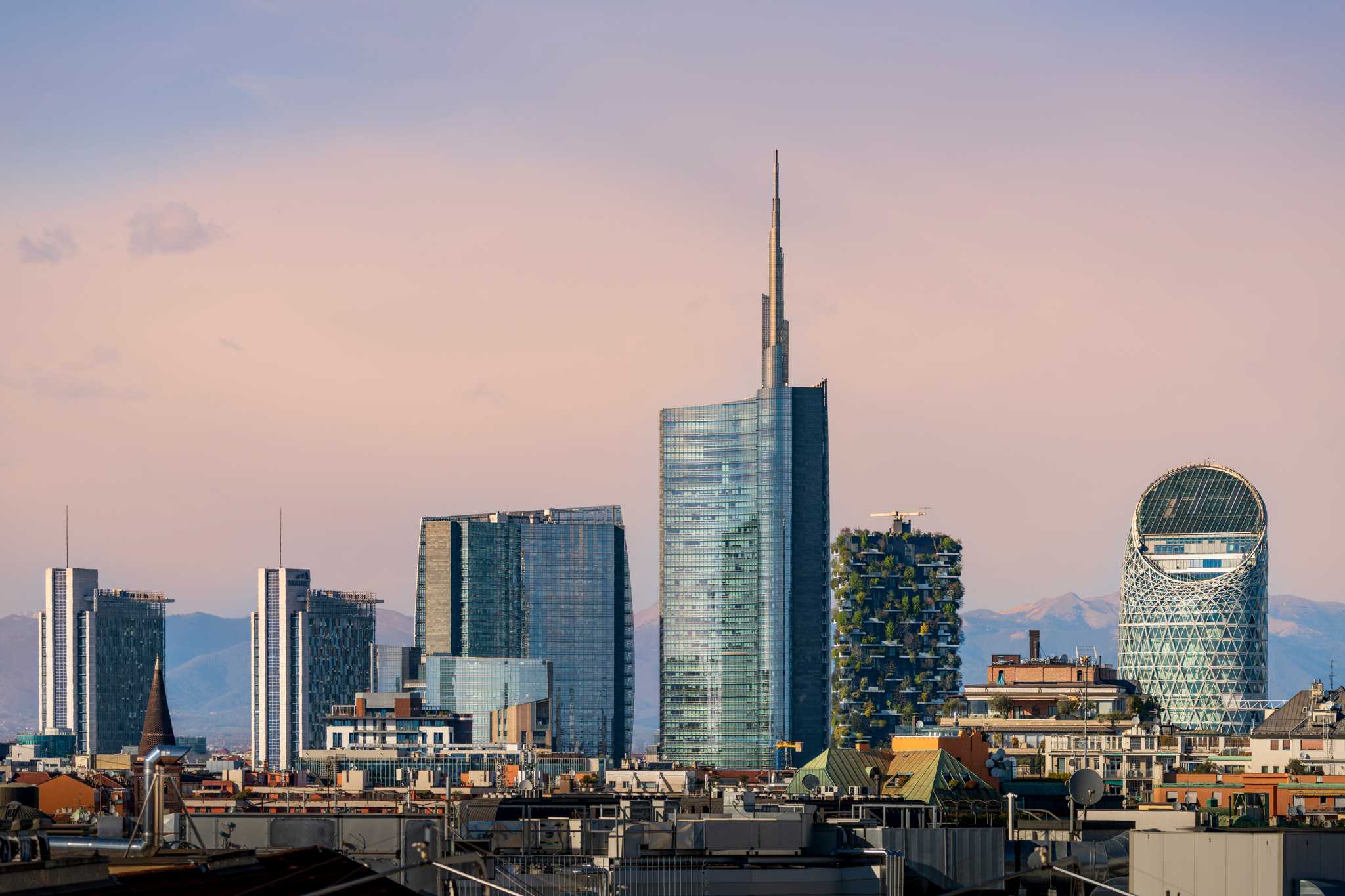 Six large, blue skyscrapers rise from Milan’s skyline against a purple sky.