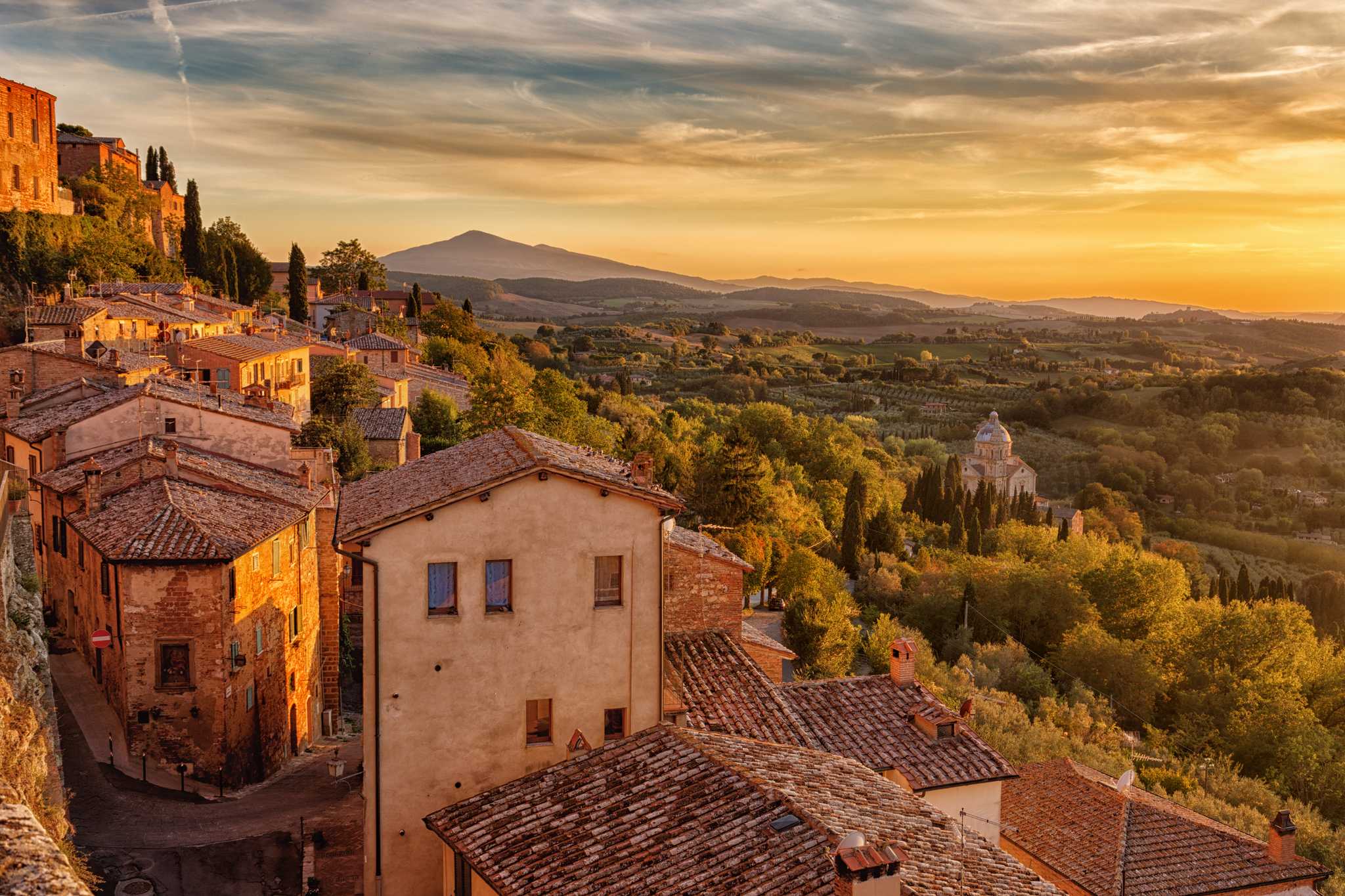 A medieval village clings to the side of a hill overlooking vast swaths of green countryside.
