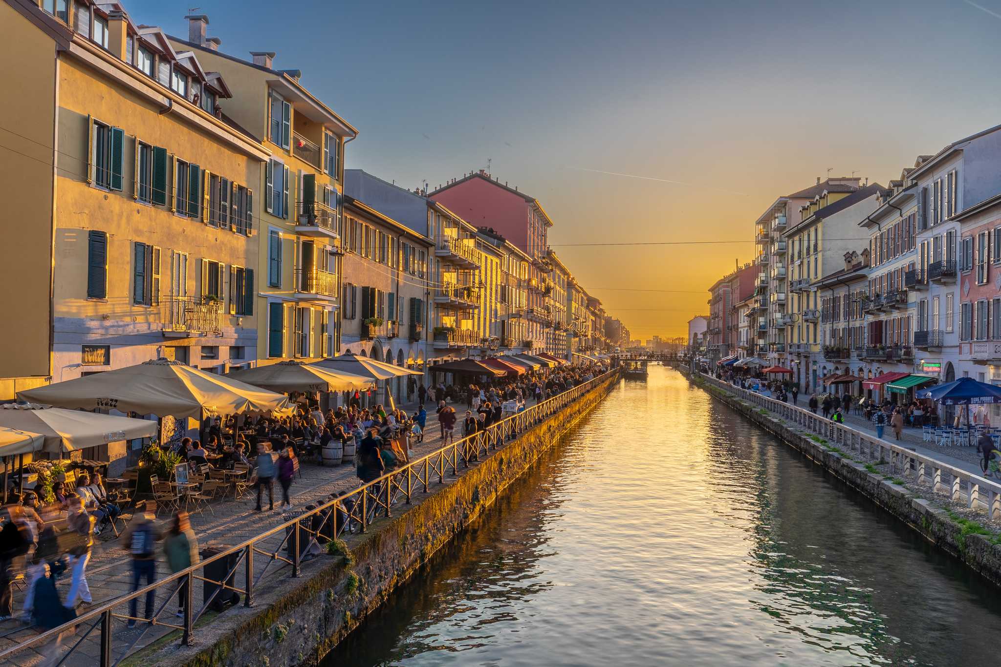 A canal with lively restaurant patios on either side of the banks at dusk.
