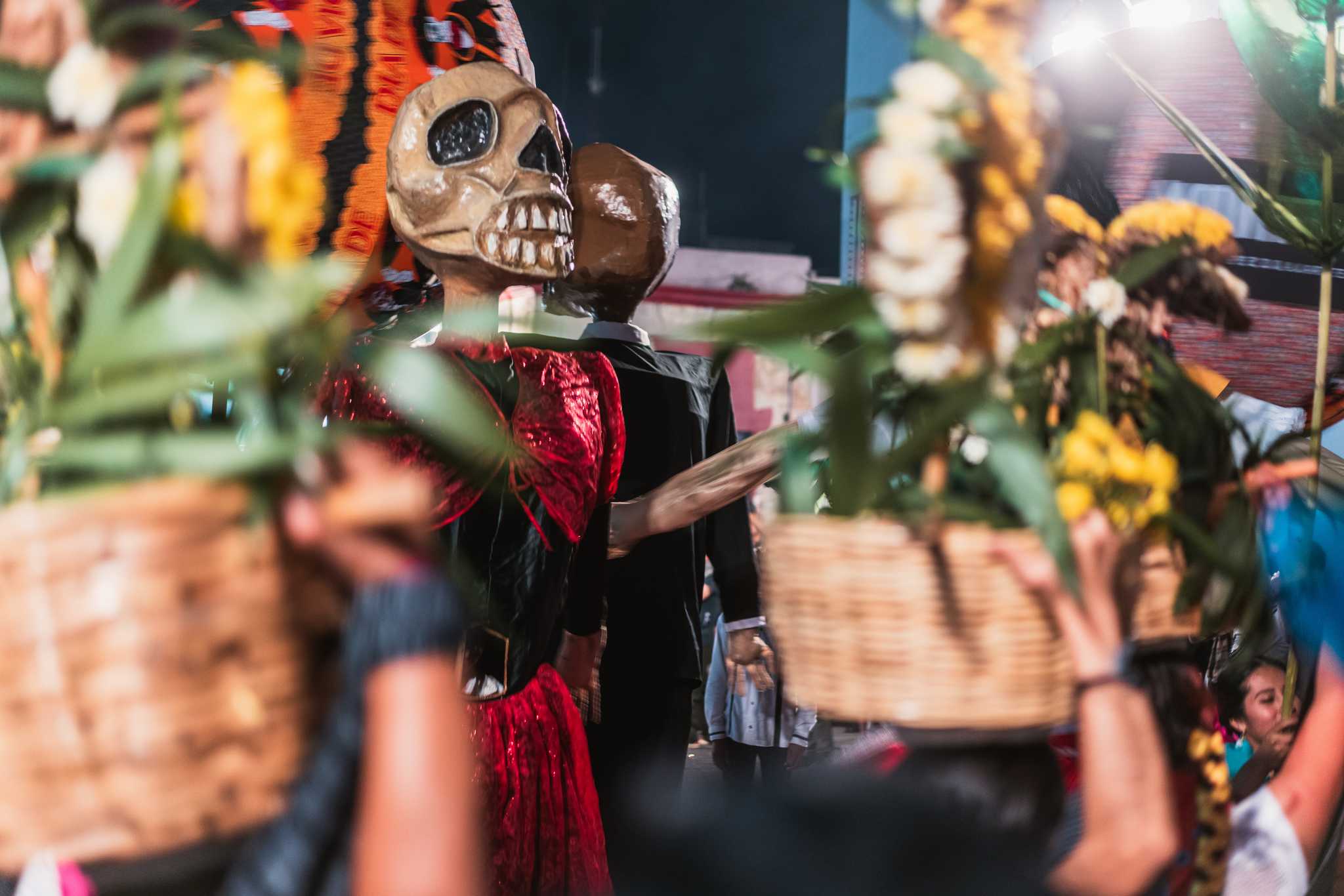 Giant skeleton puppets and flower baskets in a Día de Muertos comparsa in Oaxaca.