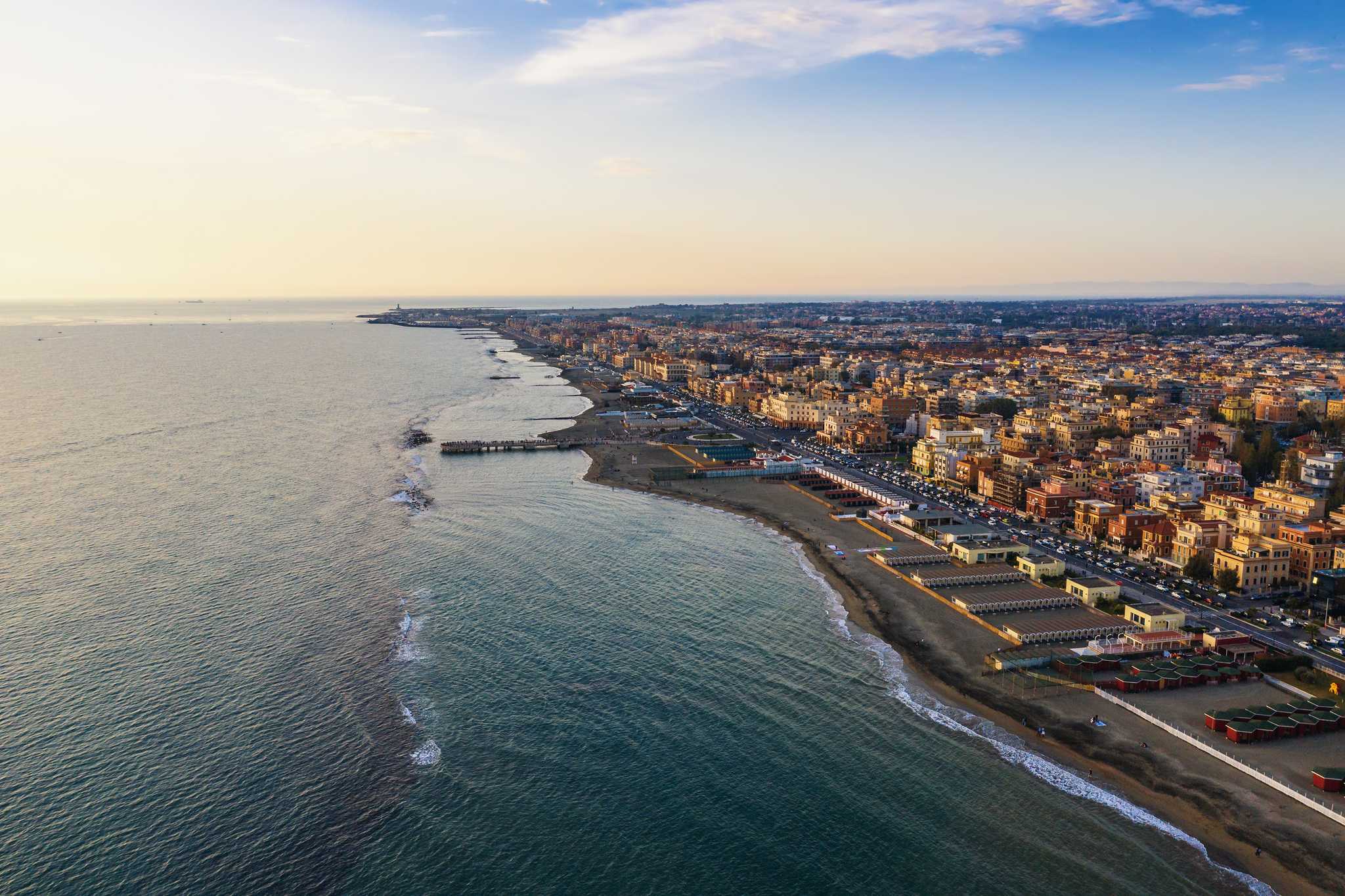 Aerial view of Ostia's coastline and beach town at golden hour.