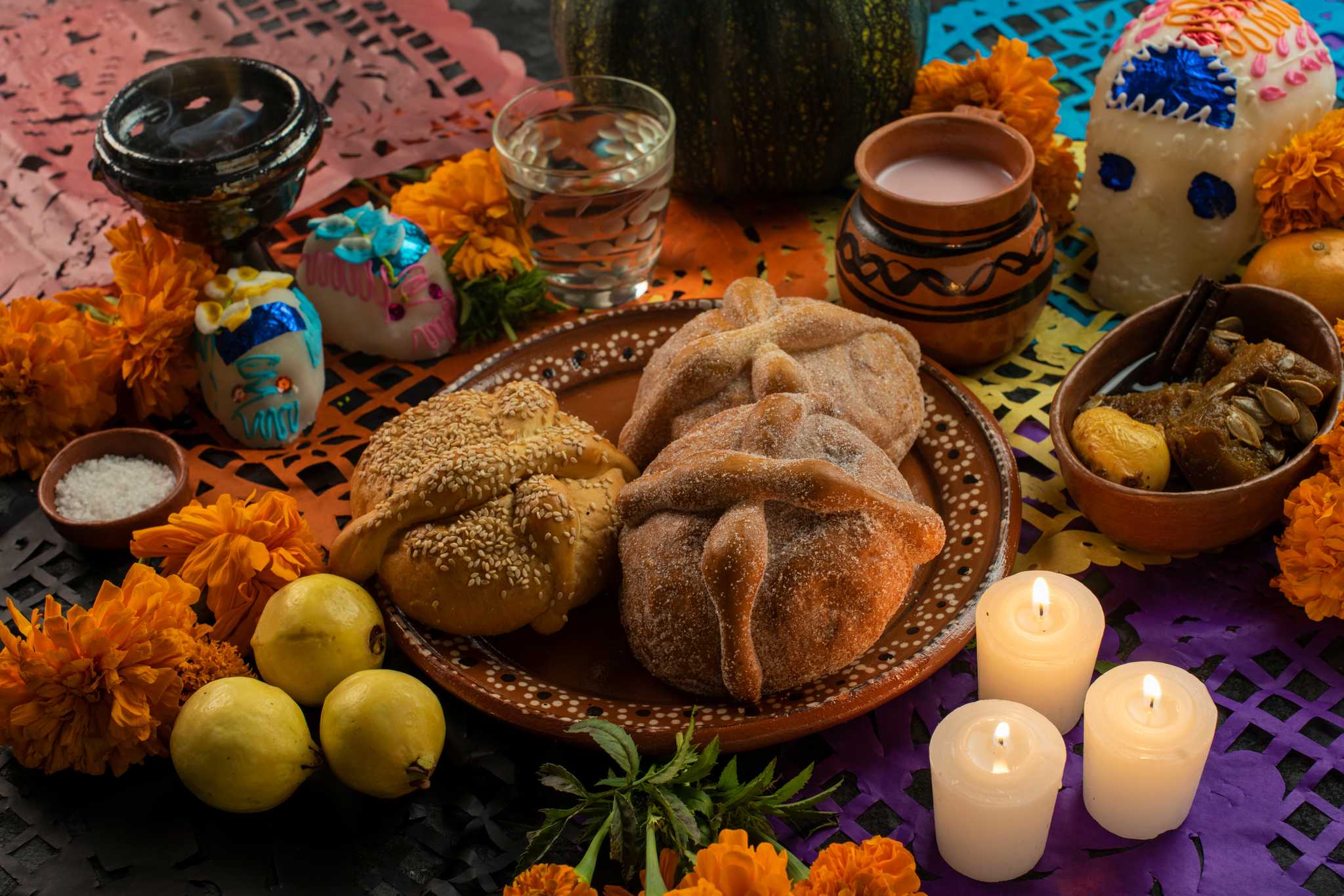 Pan de muerto on a clay plate with sugar skulls, marigolds, and candles on an ofrenda.