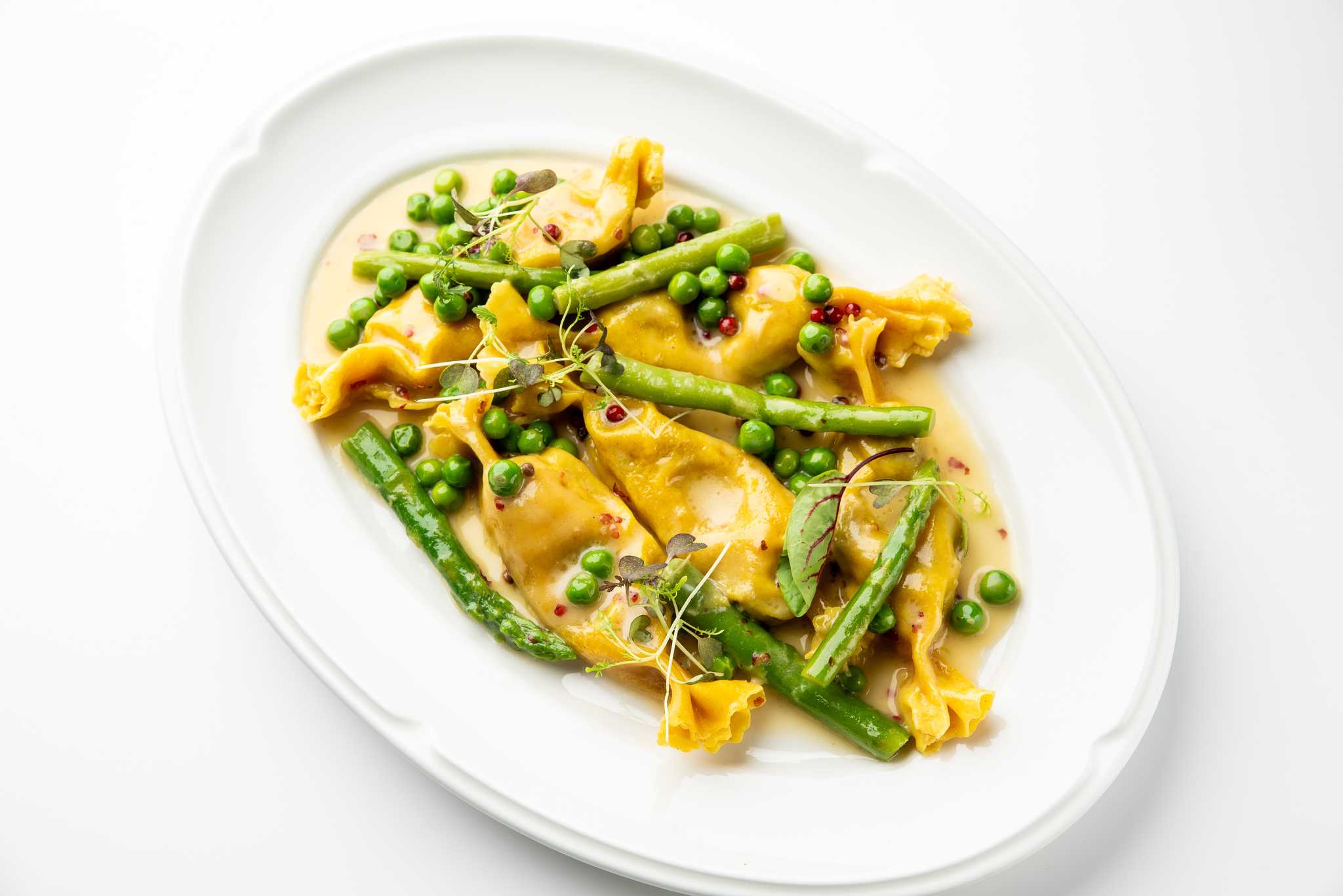 Stuffed pasta plated with asparagus, peas, and a light cream sauce.