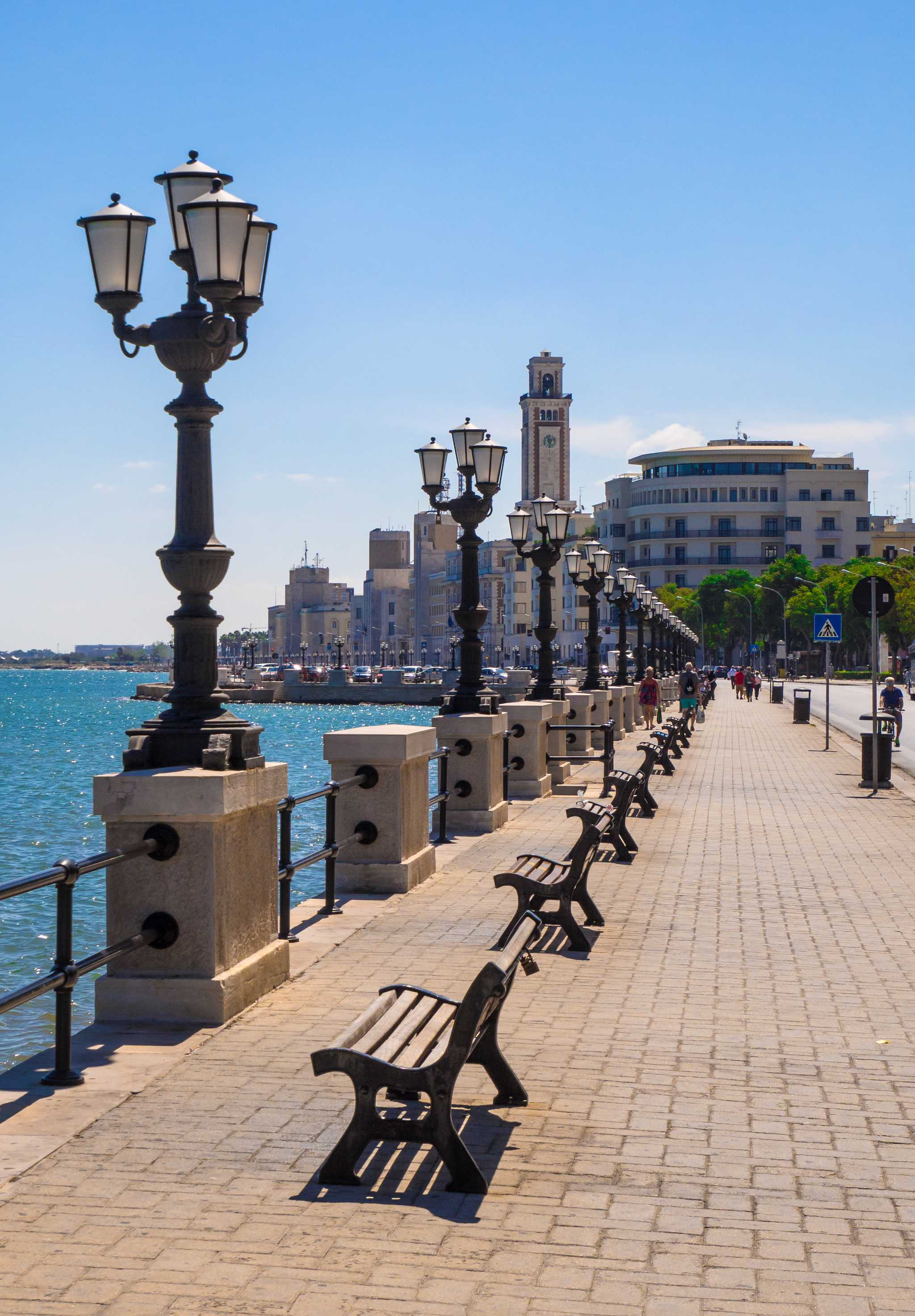Bari’s seaside promenade with benches and lampposts on the right, blue water to the left.