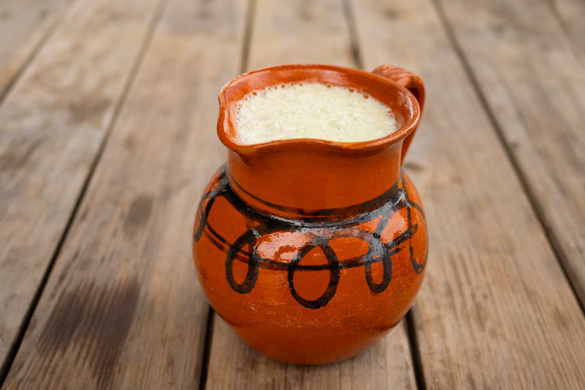 A white, foamy drink in a terracotta pitcher on a wooden table.