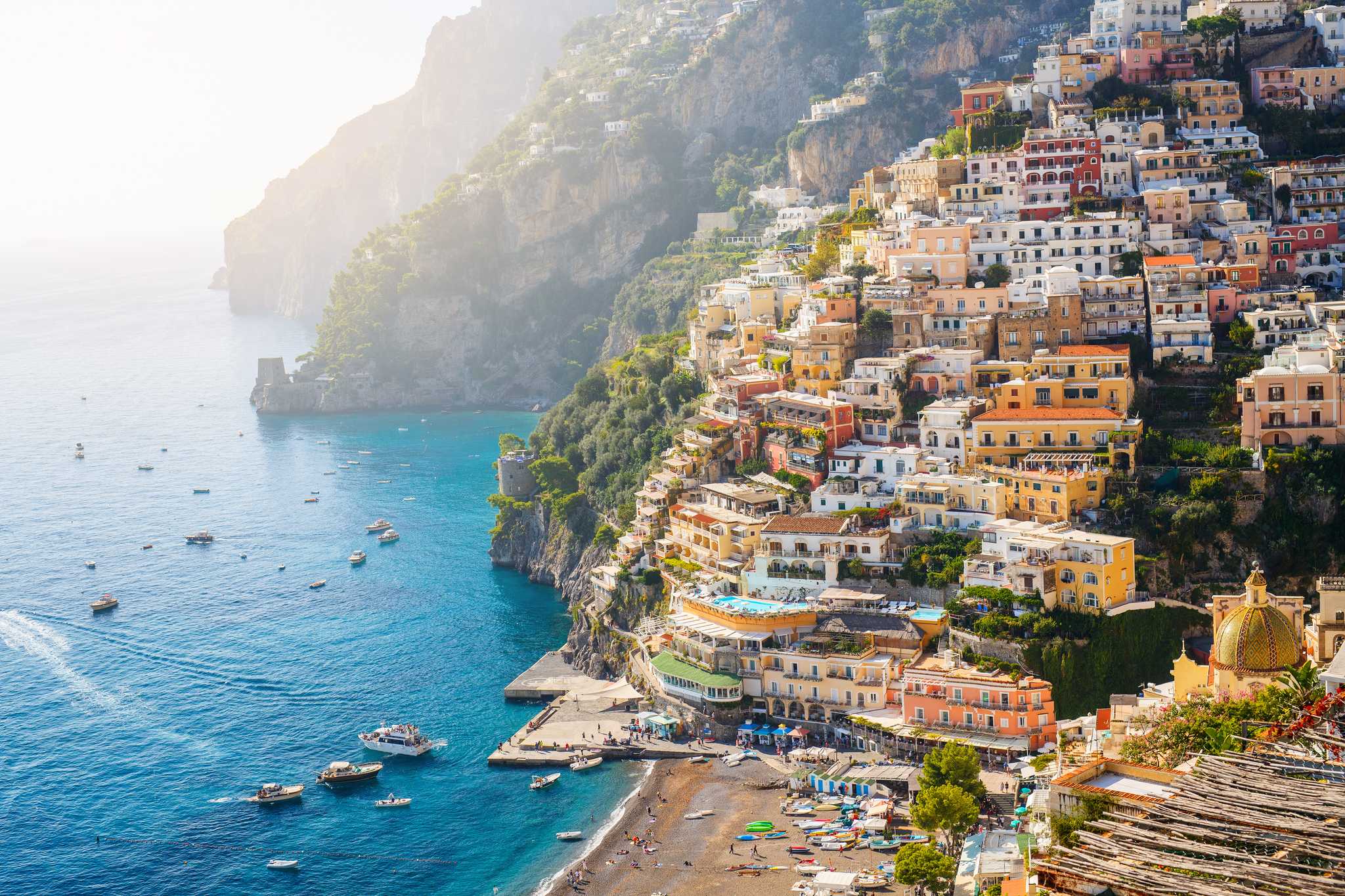 The colorful cliffside houses of Positano over sparkling blue water and boats below.