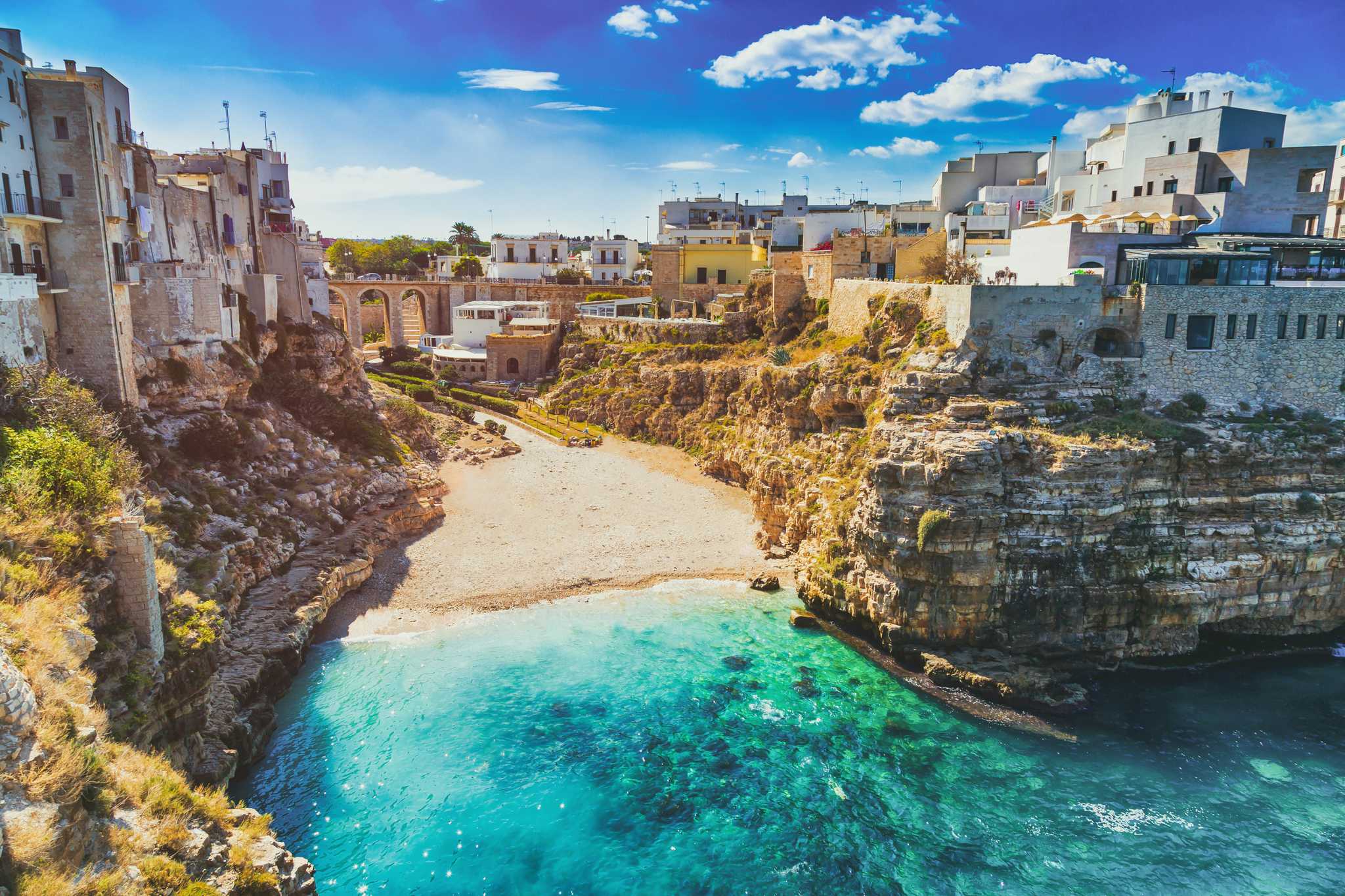 Small pebble cove in Bari between rocky cliffs topped with whitewashed houses.