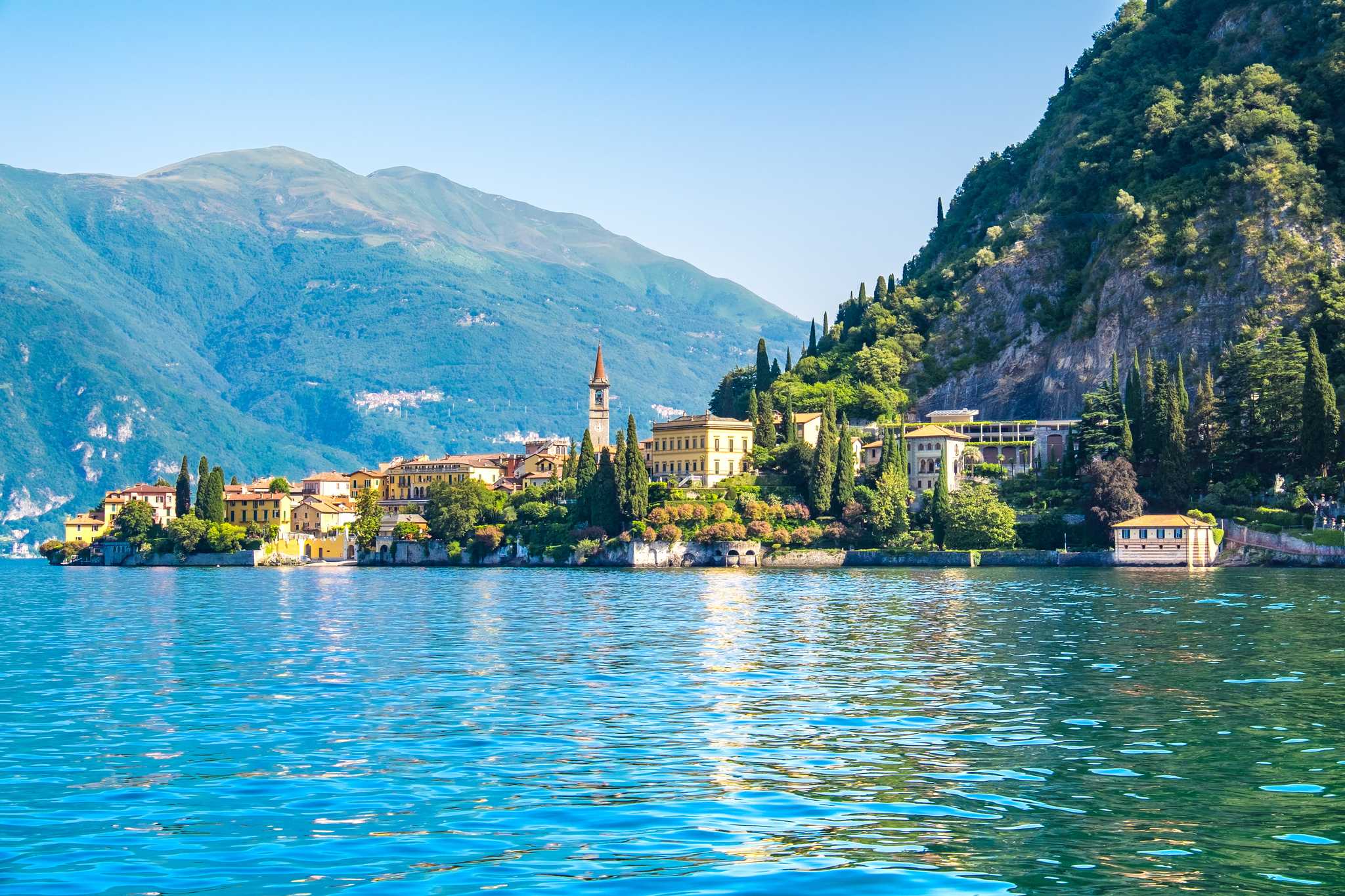 Varenna on the bank of Lake Como, with clear water in the foreground and mountains behind.