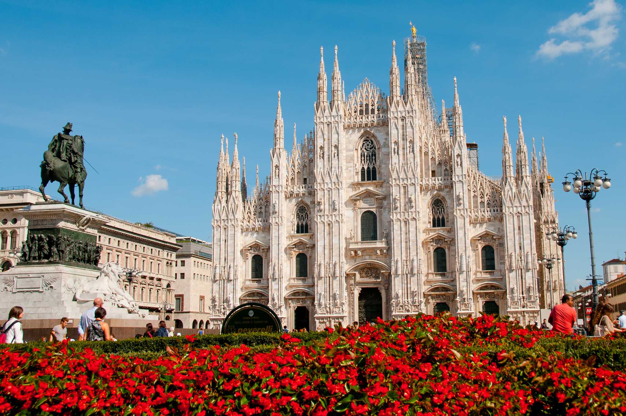 Milan’s cathedral behind red flowering bushes.