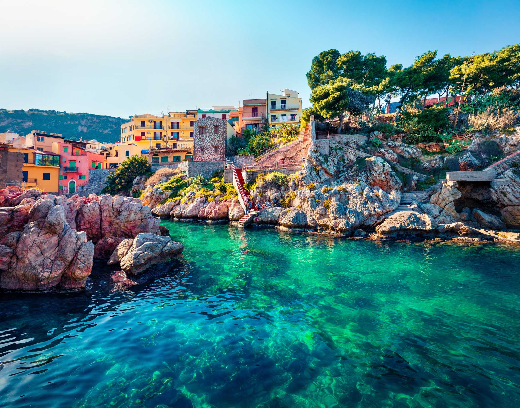 Turquoise waters of a rocky cove in Sant' Elia village, surrounded by colorful buildings.