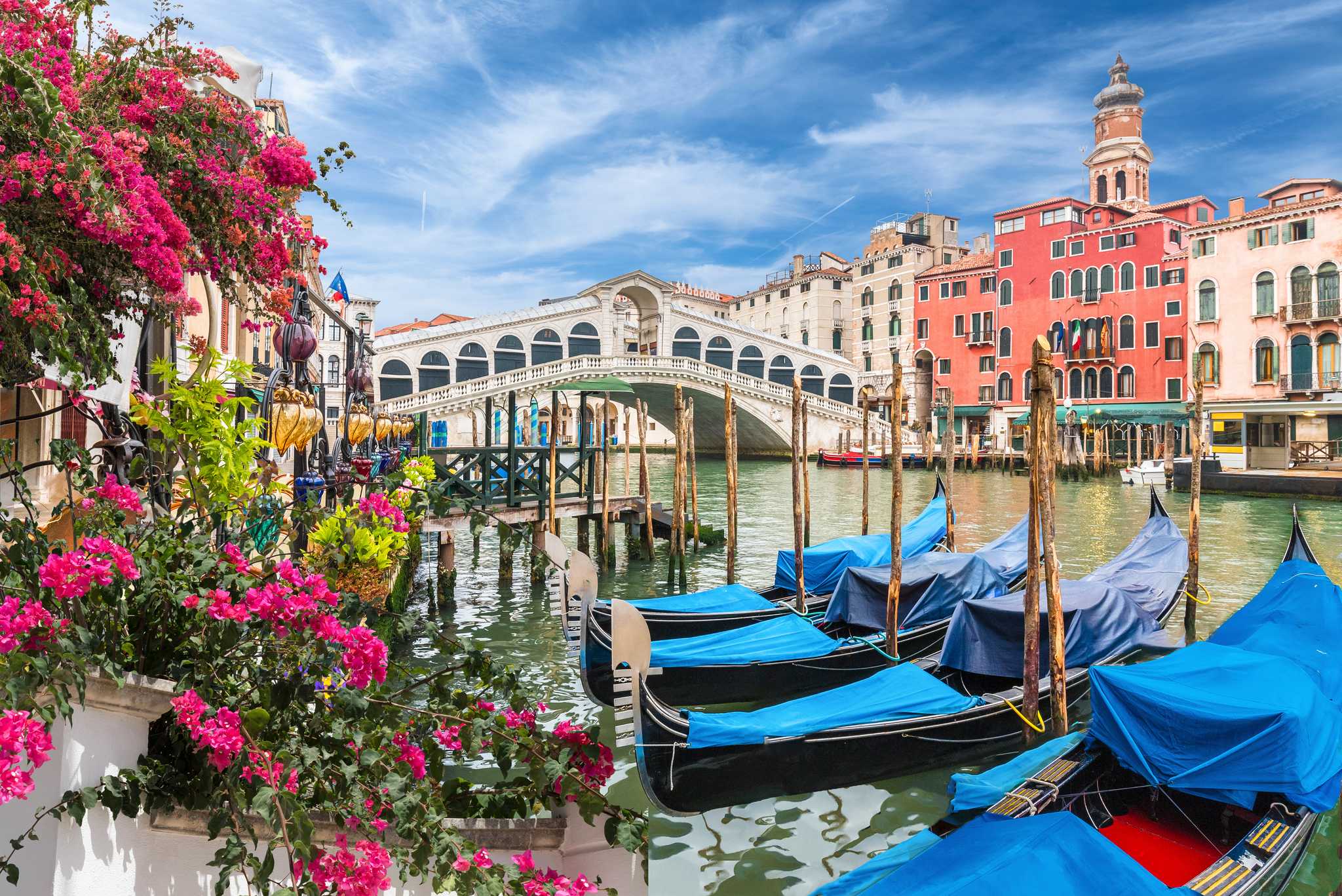 Four blue gondolas docked in a Venice canal near a stone bridge.