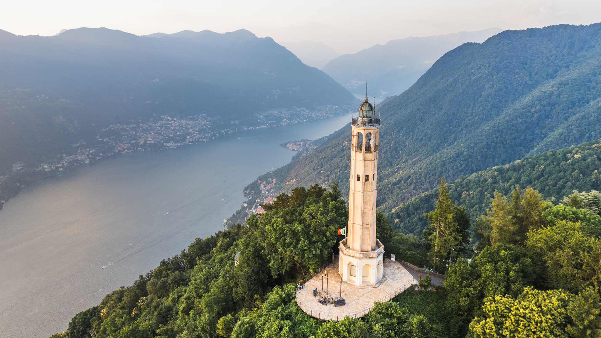 A stone lighthouse high above Lake Como, the lake winding between mountains below.