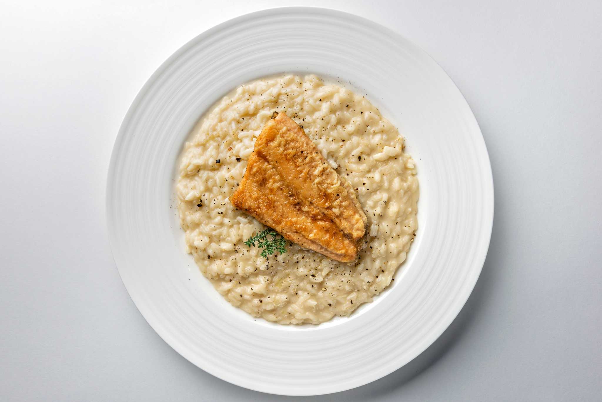 Creamy risotto topped with a pan-fried fish fillet and a herb sprig.
