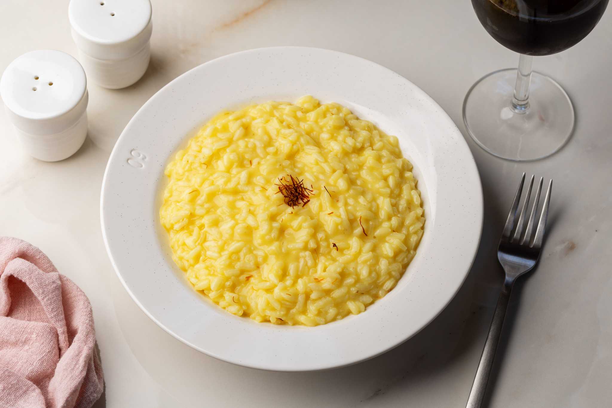 A bowl of golden risotto topped with saffron and served in a white bowl.