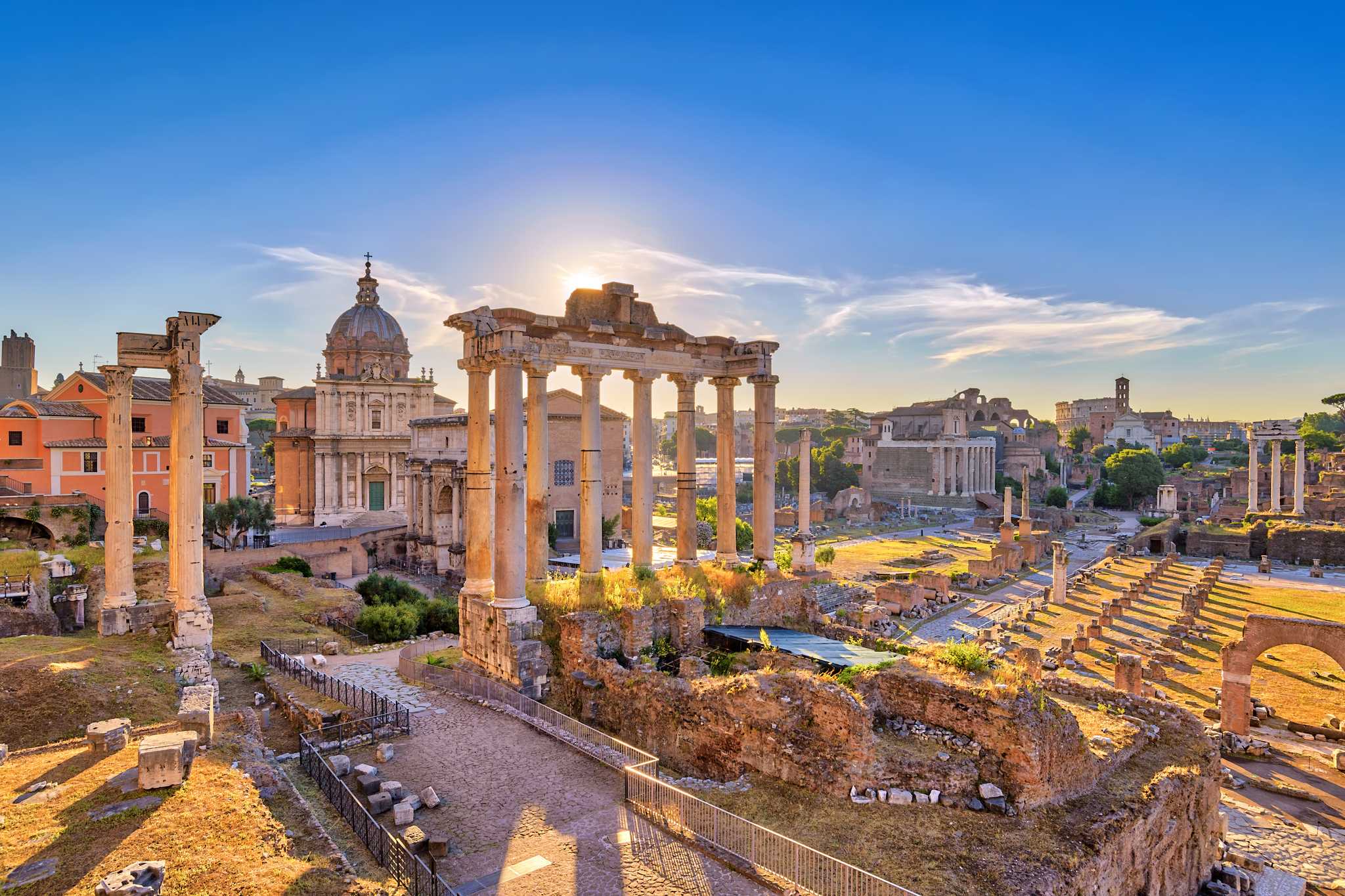 Ancient stone columns and ruins of the Roman Forum at sunrise.