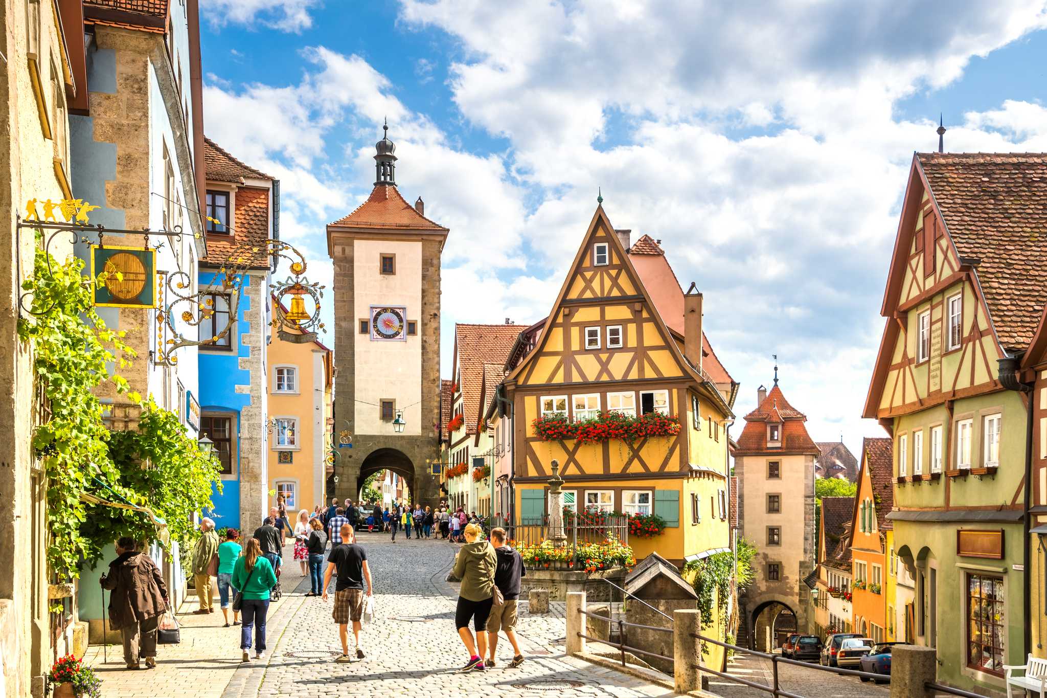 A busy cobblestoned street lined with colorful, half-timbered houses during summer.