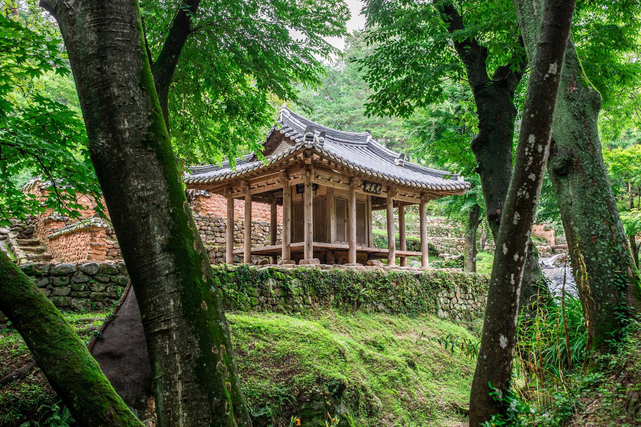A stone temple with columns in a small courtyard surrounded by trees.