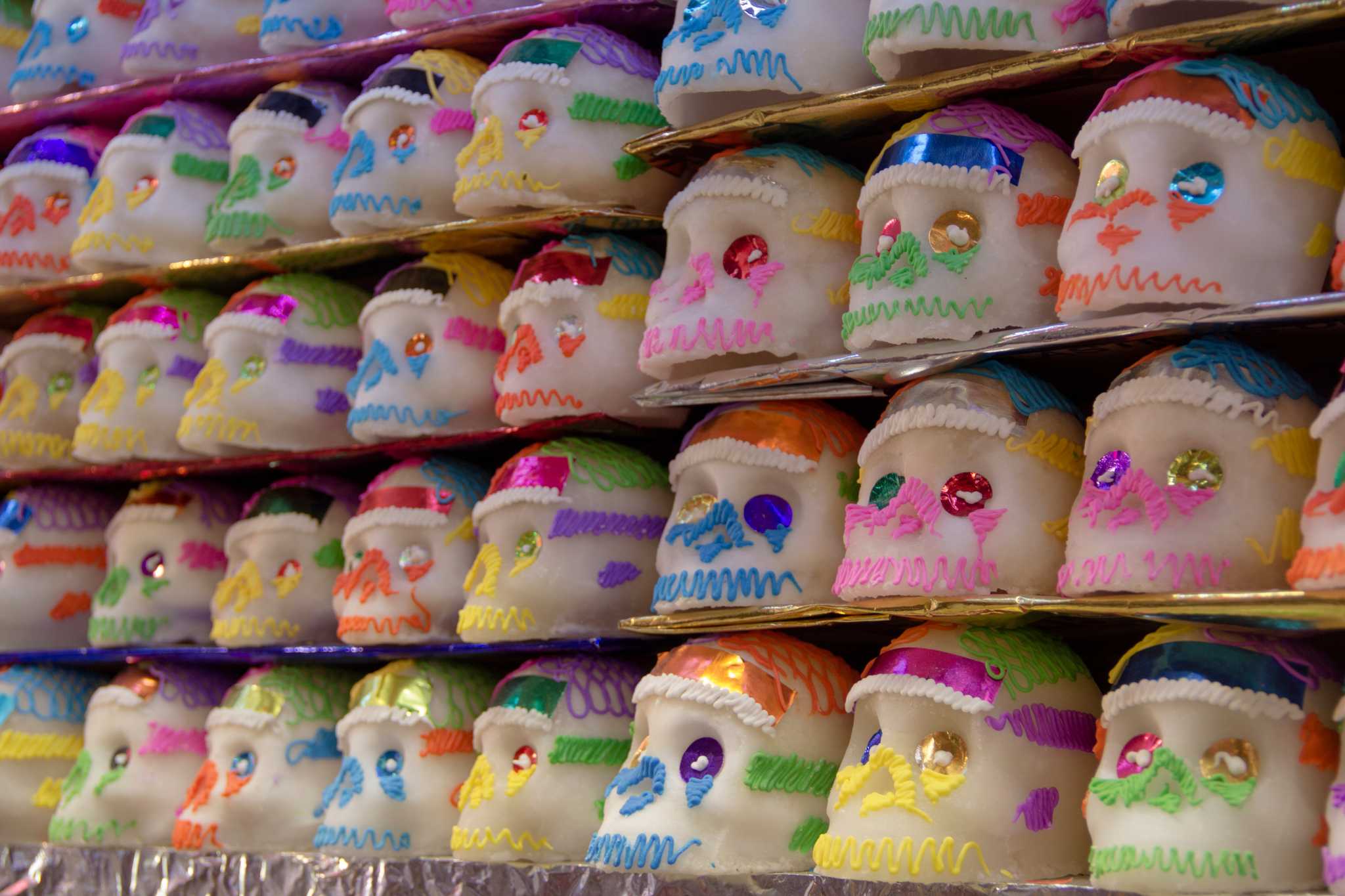 Rows of sugar skulls with bright piped icing and foil details for Día de los Muertos.