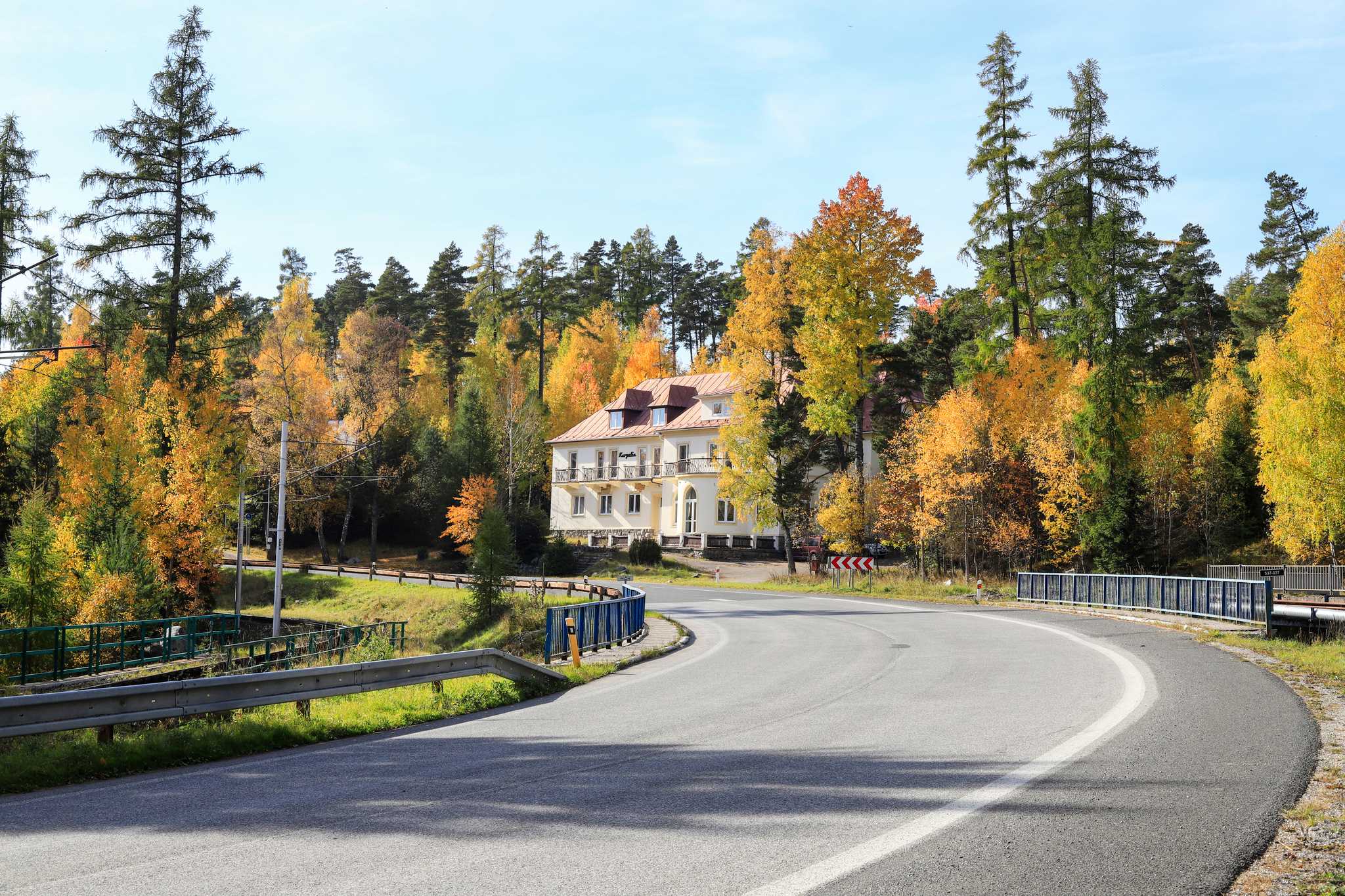 A white Austro-Hungarian building along a road lined with trees changing colors for fall.