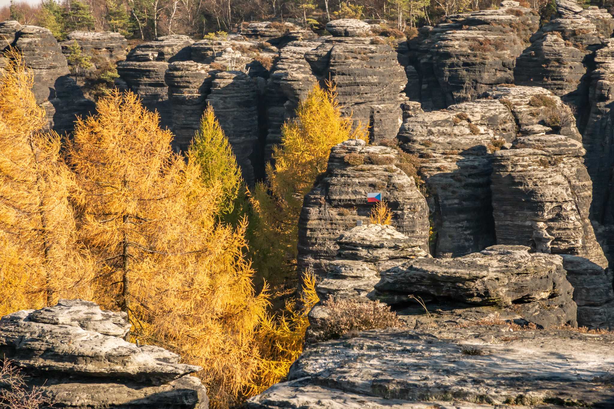 Sandstone rock towers jut out of the earth, with a Czech flag on one of them.