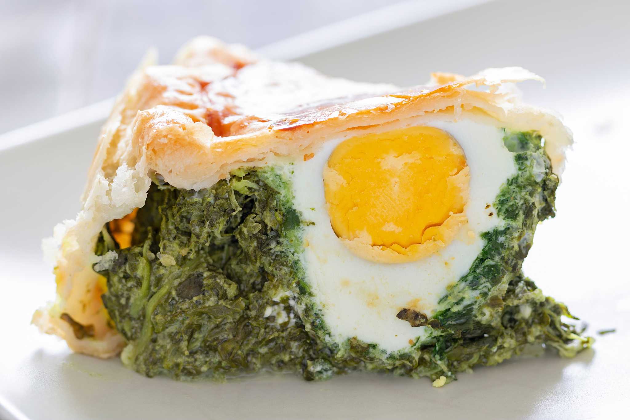 Slice of savory pie with spinach filling and a whole boiled egg.