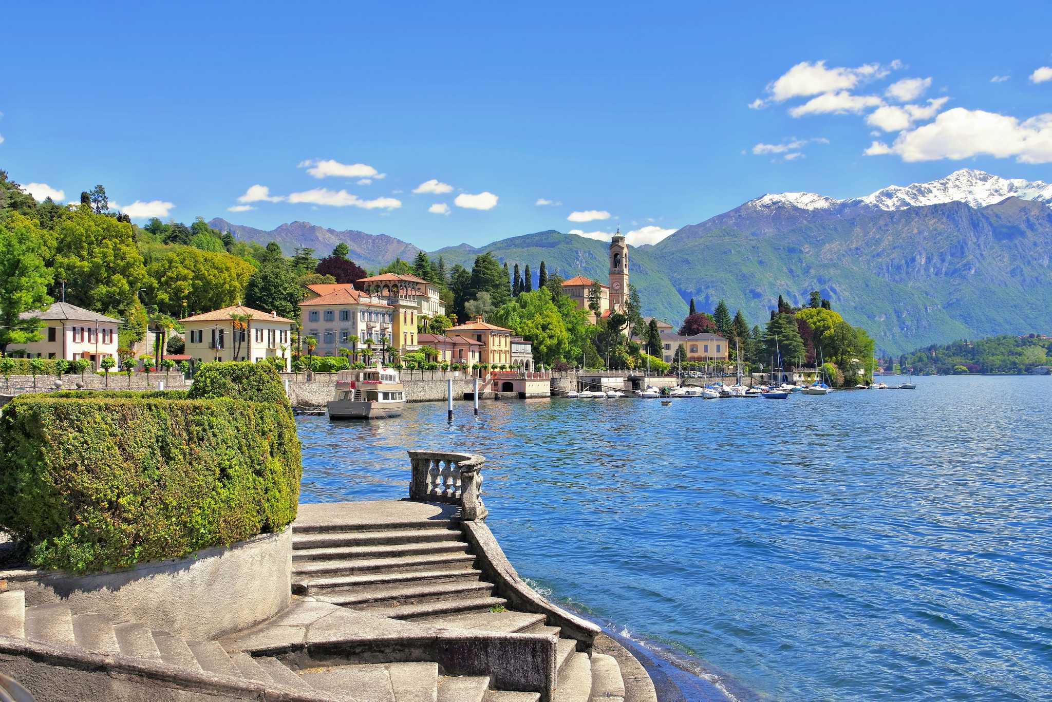 Curved stone steps to Lake Como at Tremezzo, with villas and a bell tower below snowy peaks.