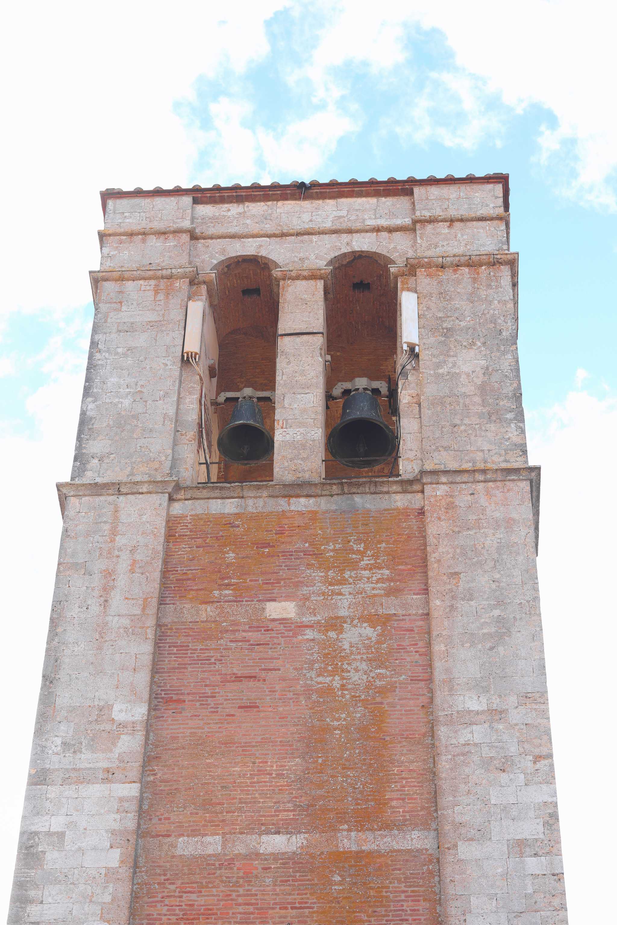 Close-up of Montepulciano’s bell tower, a light red stone structure with two aged bells.