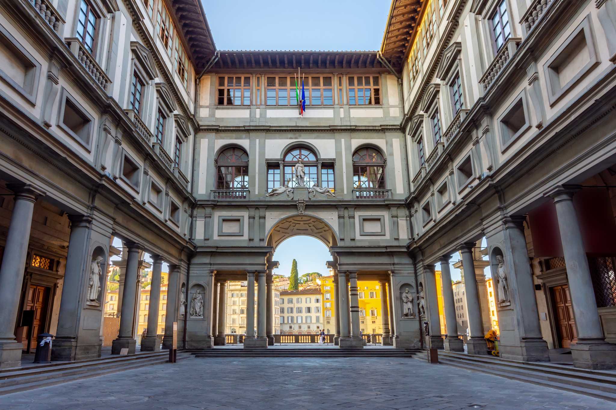 The grand courtyard of the Uffizi, flanked by marble columns and shadows.