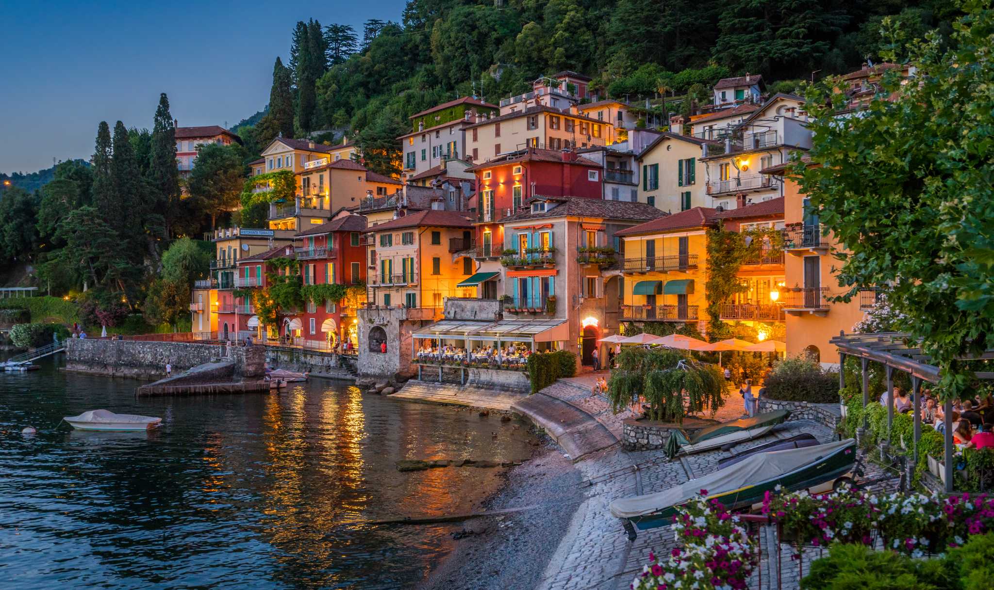 Varenna's colorful houses glowing above a small harbor on Lake Como at dusk.