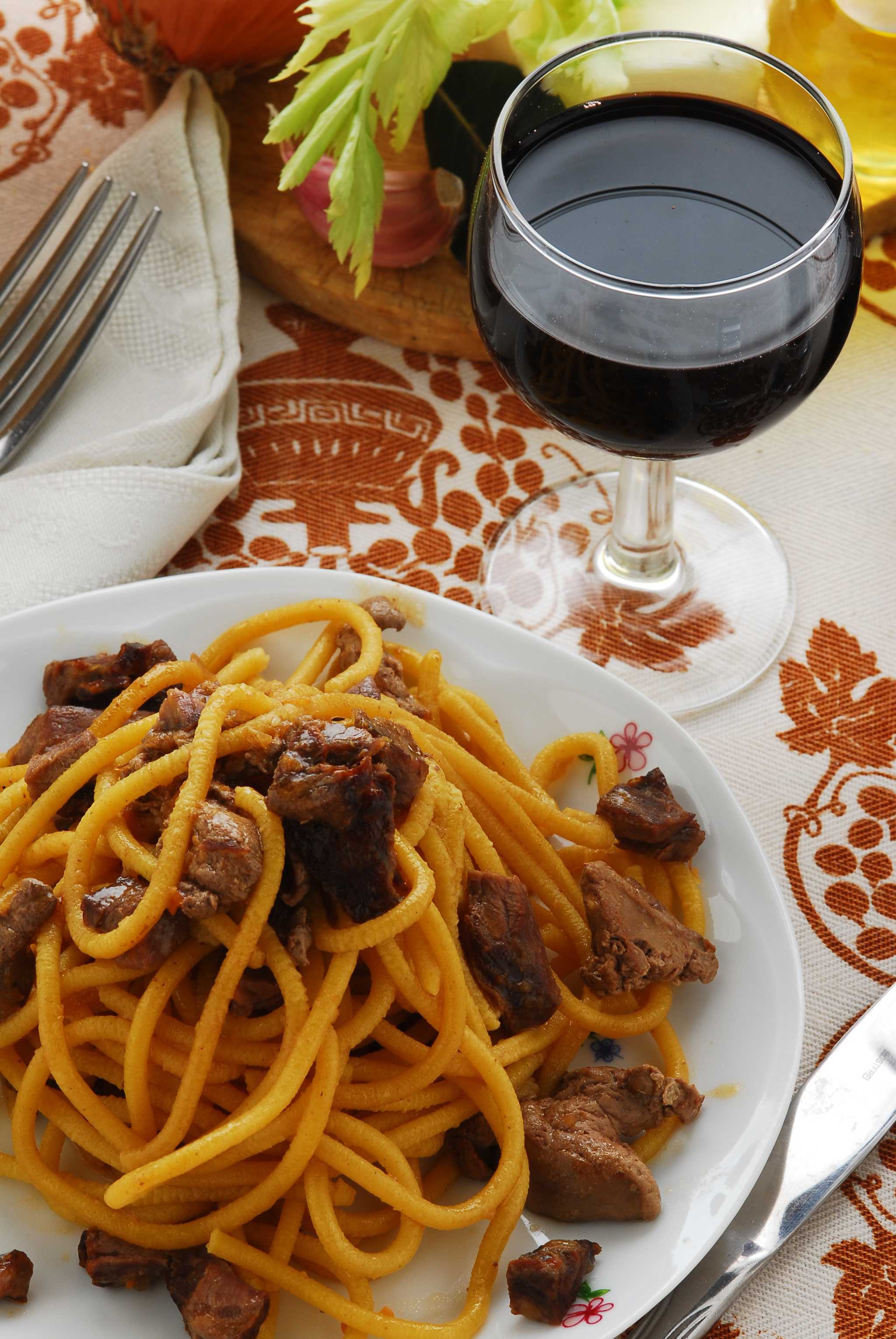 Venetian bigoli pasta with duck ragù on a white plate, served with a glass of red wine.