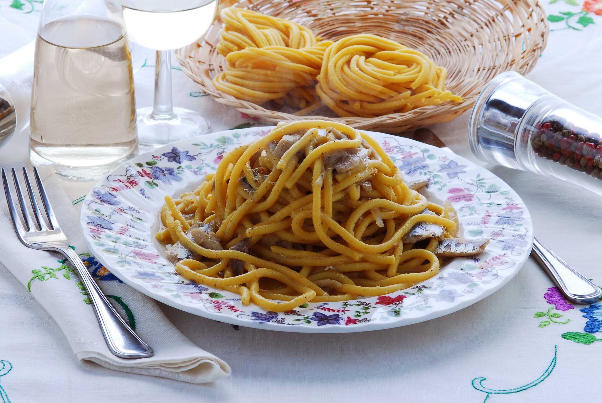 Venetian bigoli in salsa pasta with anchovy sauce on a floral plate, with white wine and more pasta.