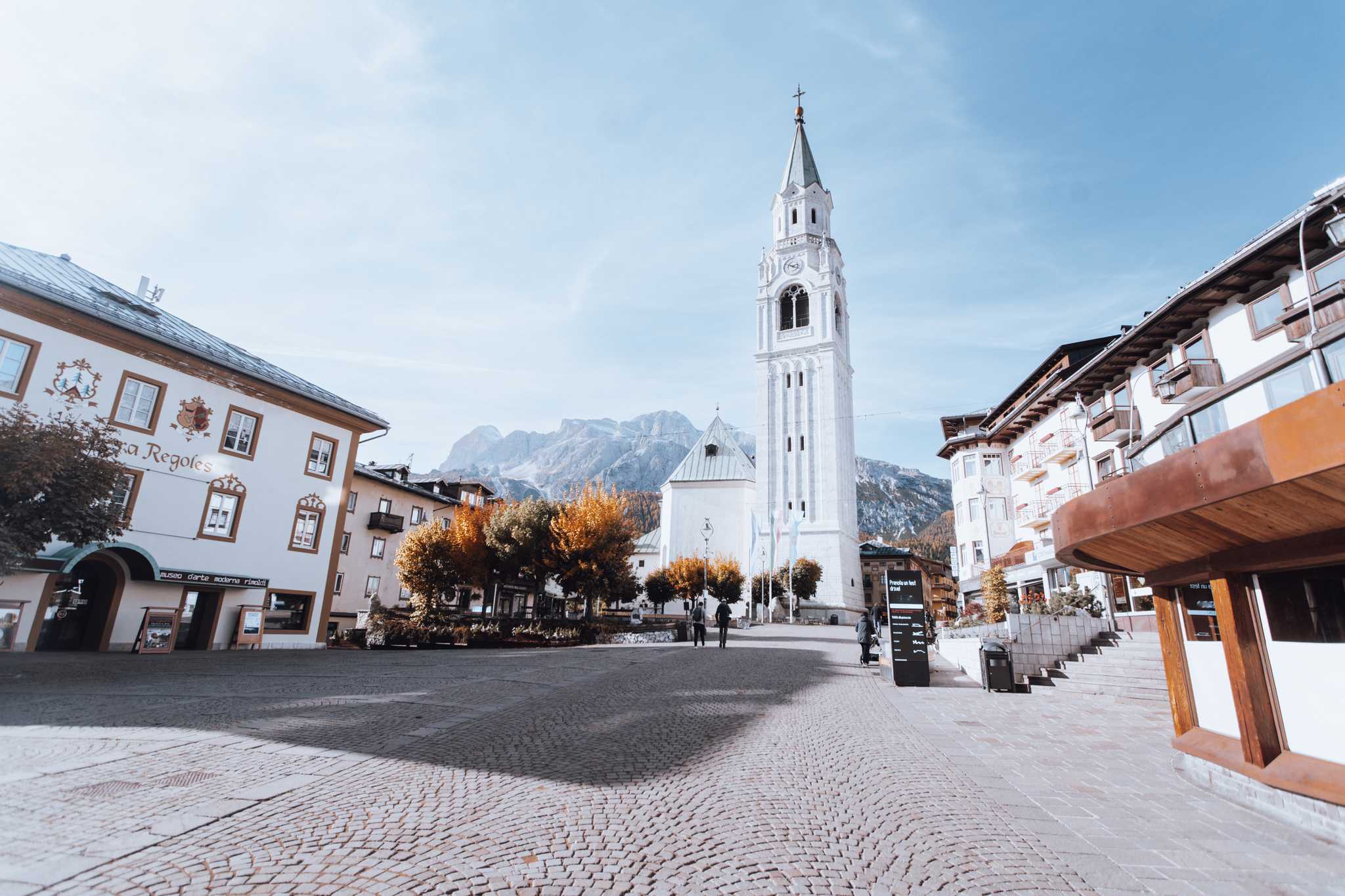 Cobbled town square in Cortina d'Ampezzo with a white bell tower and Dolomite peaks in the background.