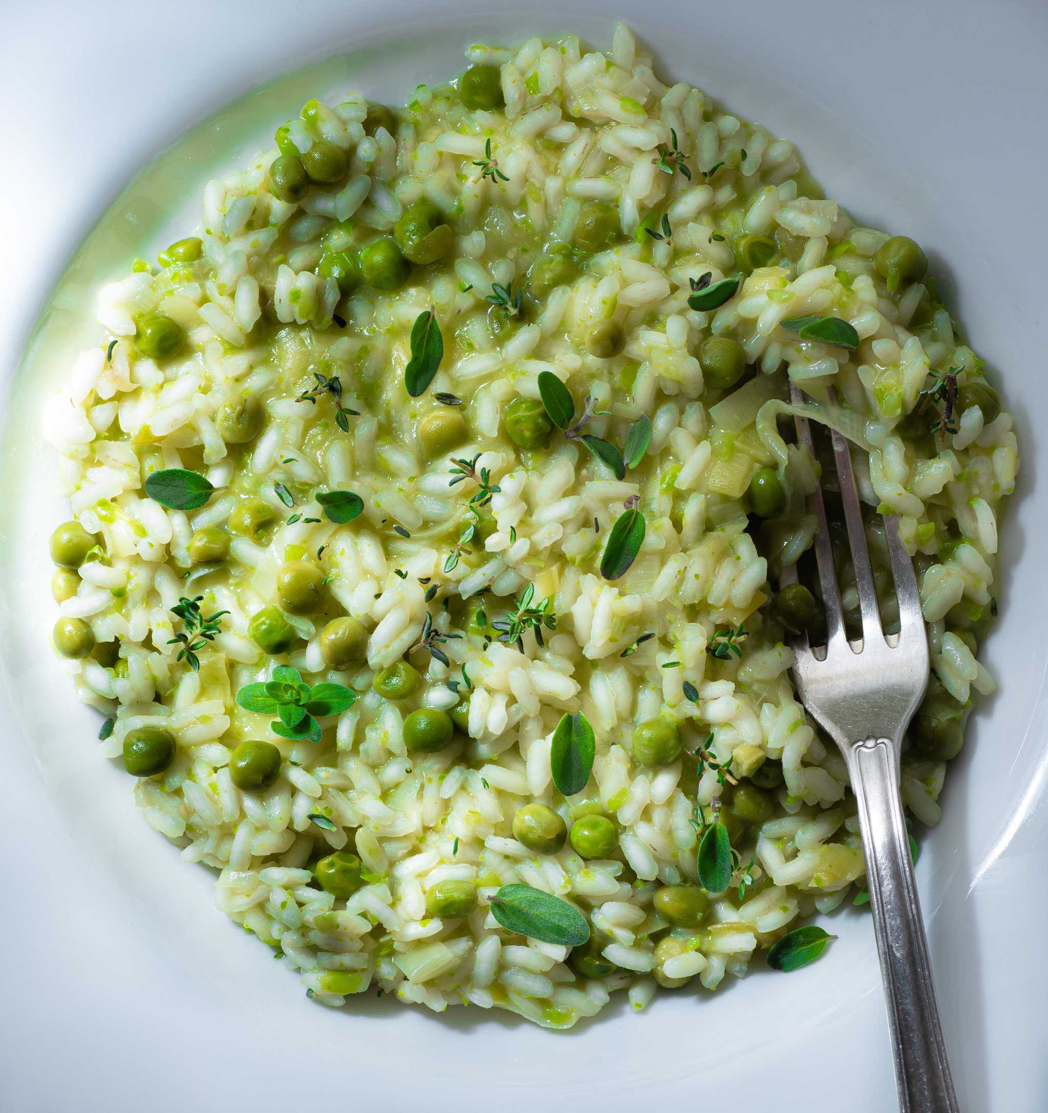 Venetian risi e bisi, creamy rice with green peas and herbs, on a white plate with a fork.