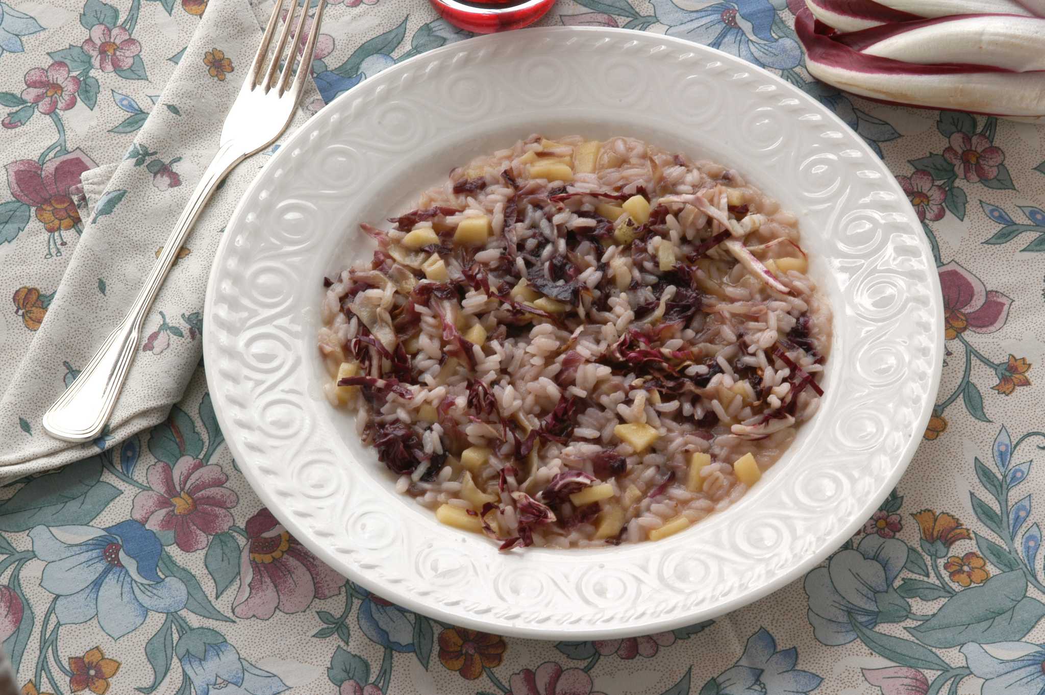 Radicchio risotto with red chicory in a white embossed bowl, on a floral cloth with a fork.