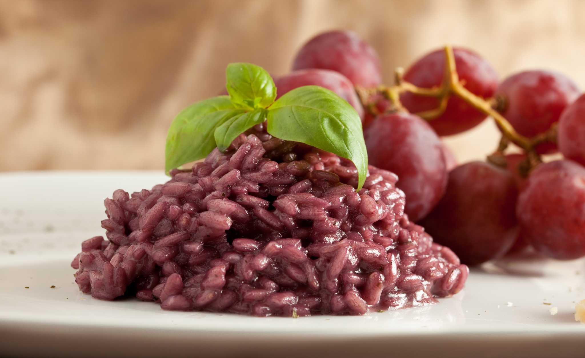 Purple red-wine risotto topped with fresh basil, with a bunch of red grapes alongside.