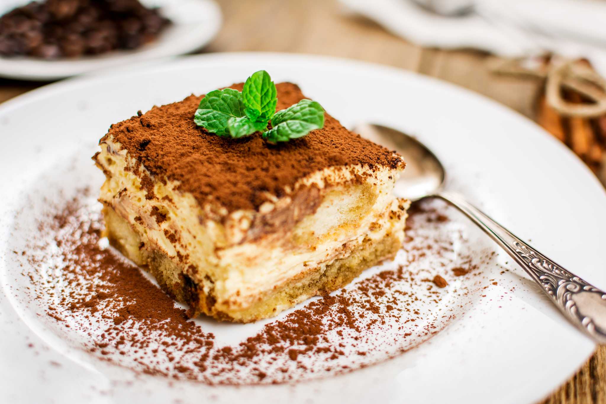 Tiramisu on a white plate, sprinkled with powdered sugar and topped with a mint sprig.