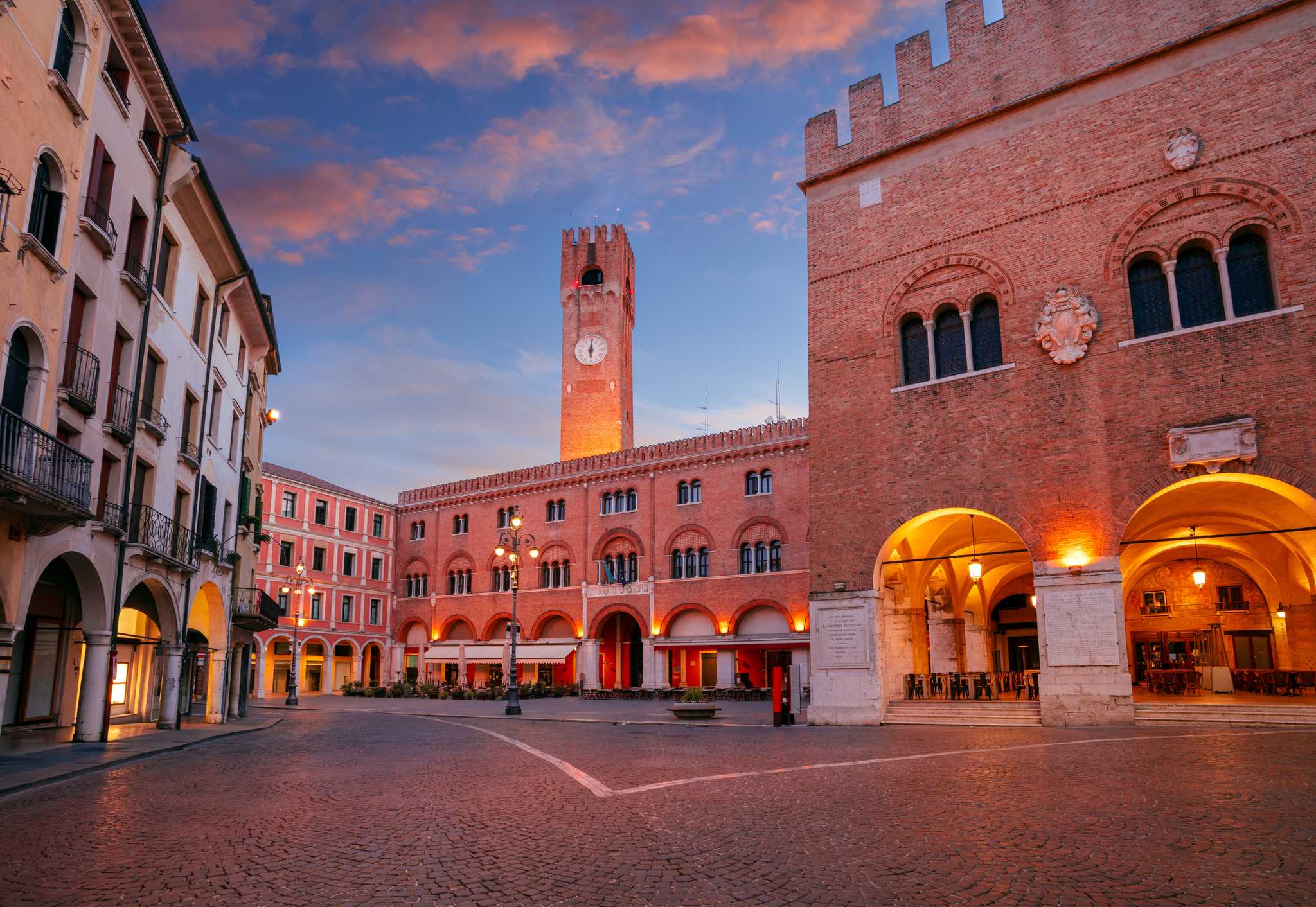 A cobbled square in Treviso, with red brick buildings, and a clock tower in the background.