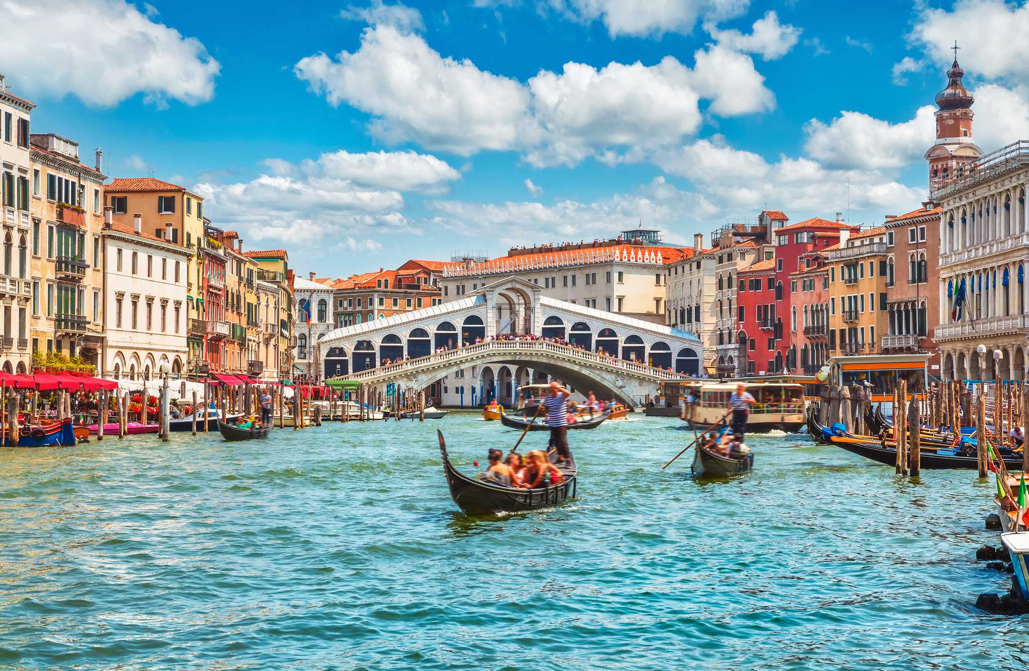 The rivers of Venice, with a gondola in the foreground and the Ponte di Rialto, a grand, white bridge, in the background.