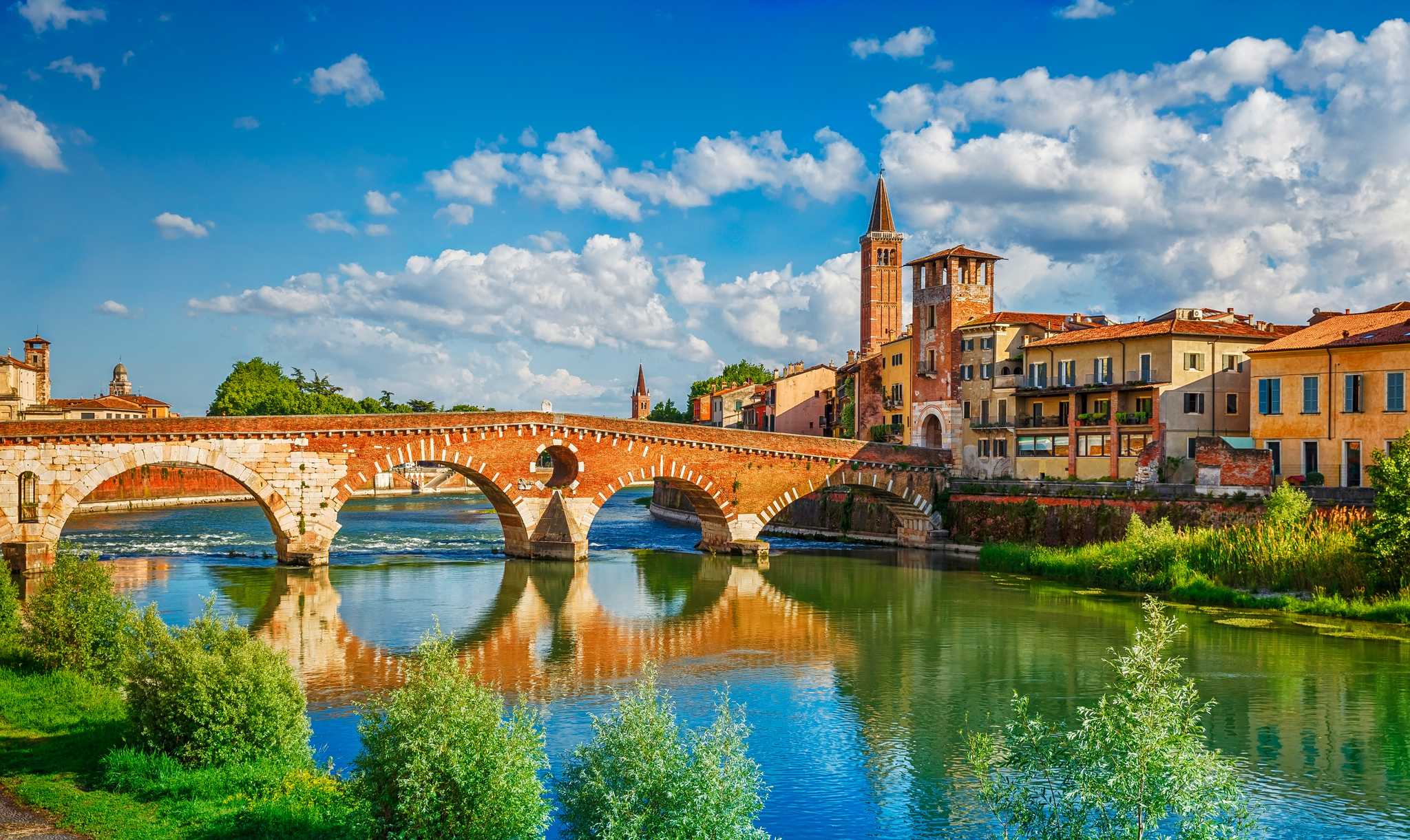 The Ponte Pietra stone bridge over the Adige River in Verona, with a bell tower behind it.