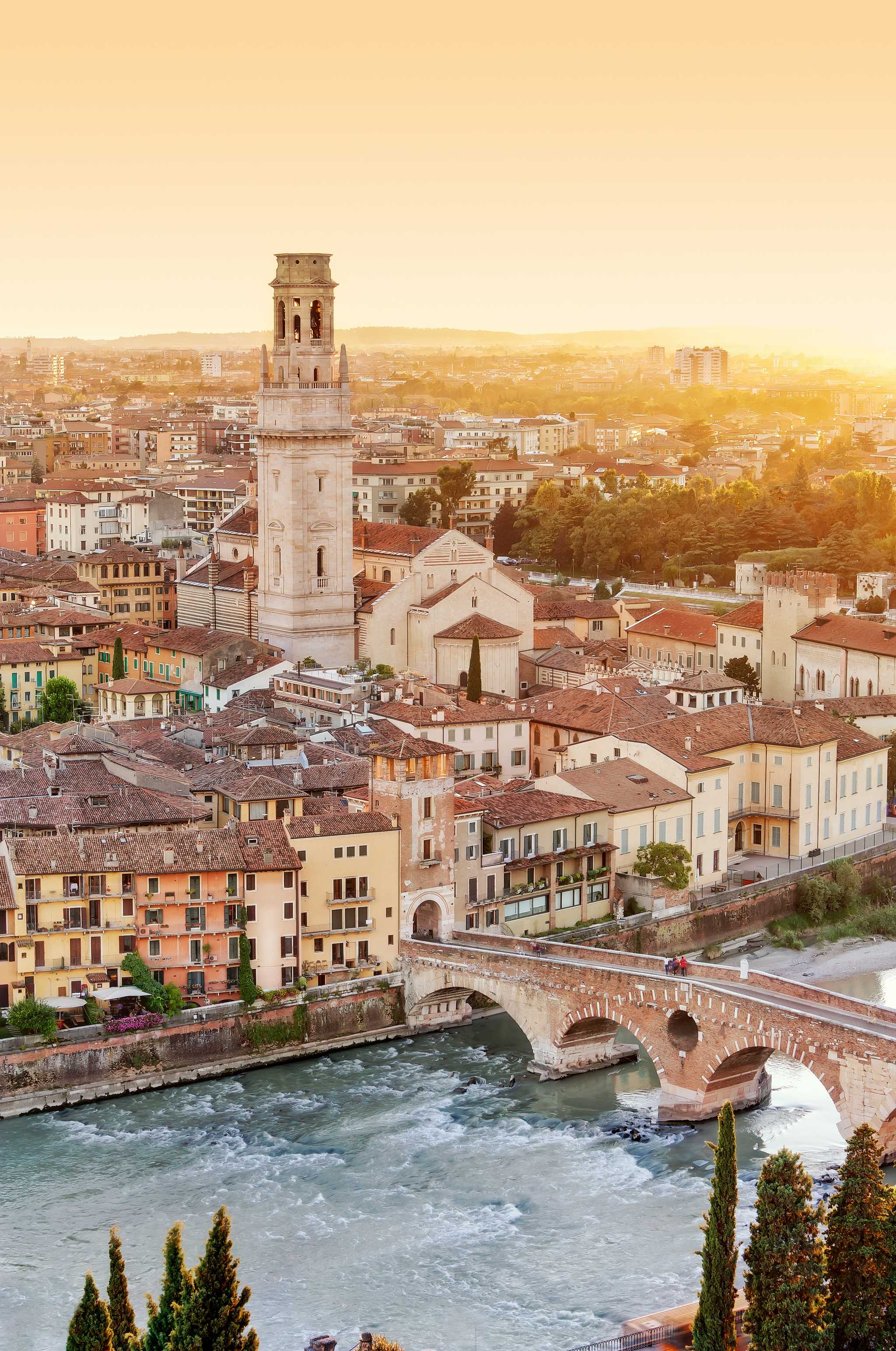 High view of Verona skyline and the Ponte Pietra arch bridge during a golden sunset.