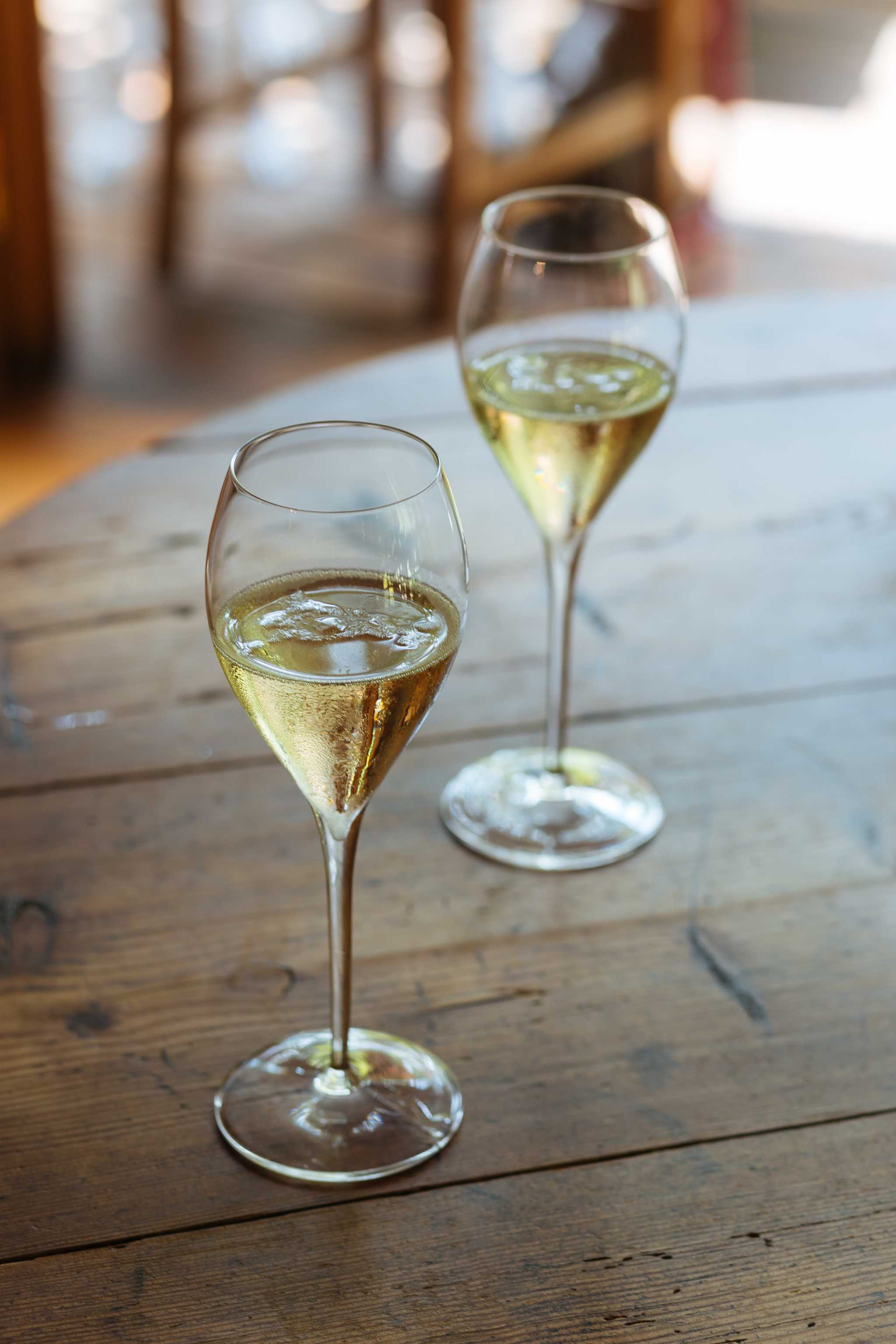 Two glasses of sparkling white wine on a wooden table.