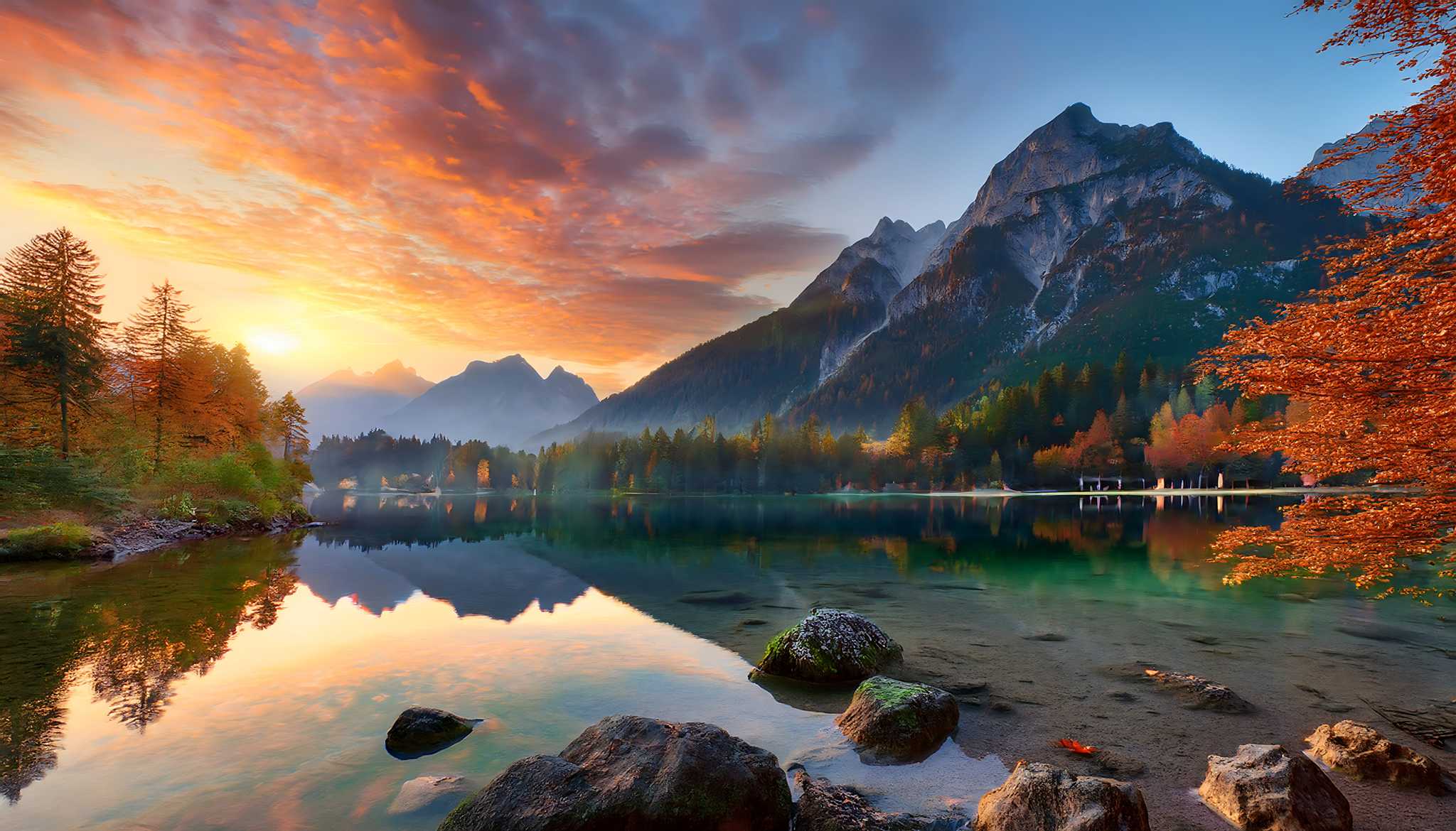The sun rises over a foggy scene of a lake with mountains in the background.